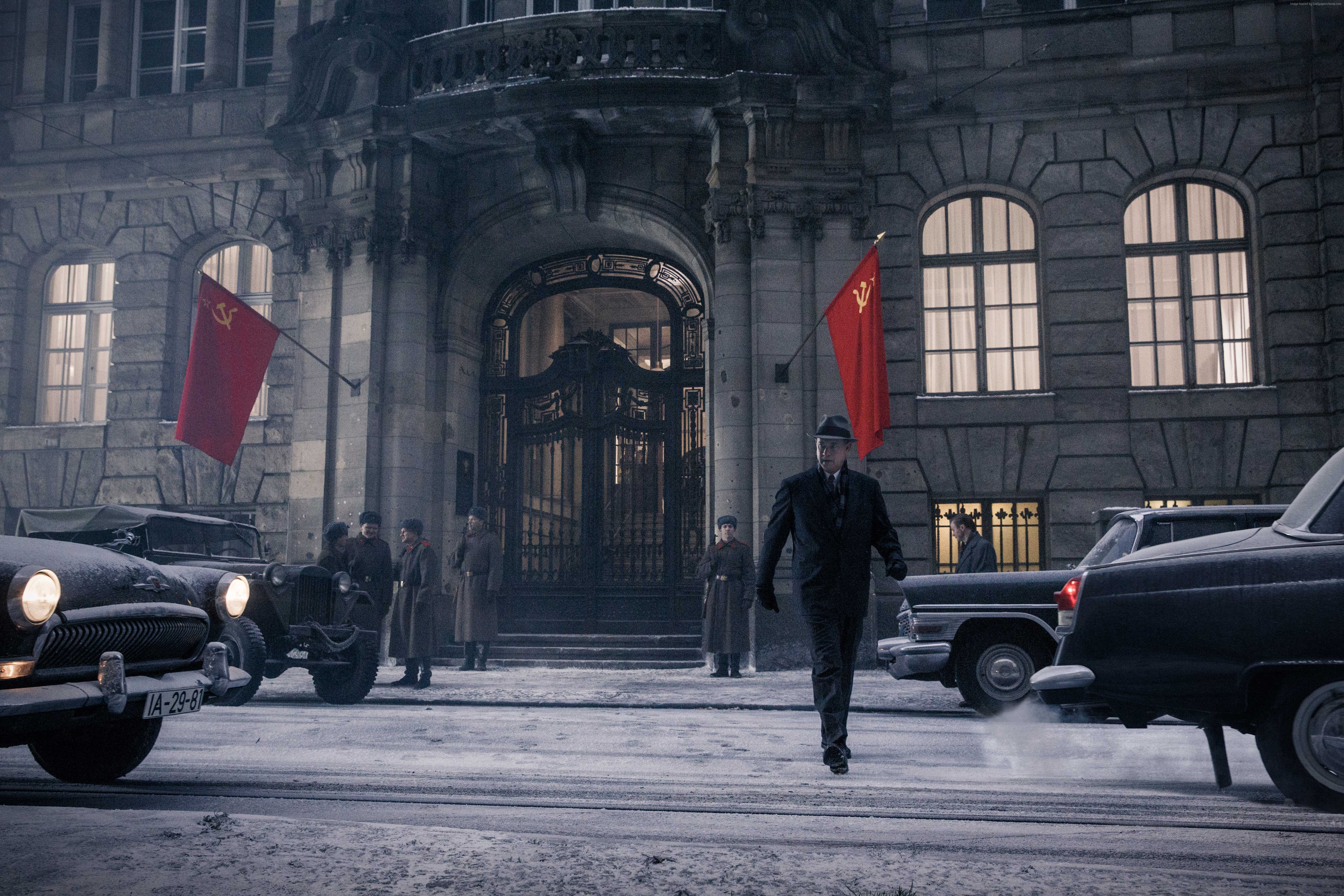 Man in suit walking in front of building with Soviet flags HD Wallpaper