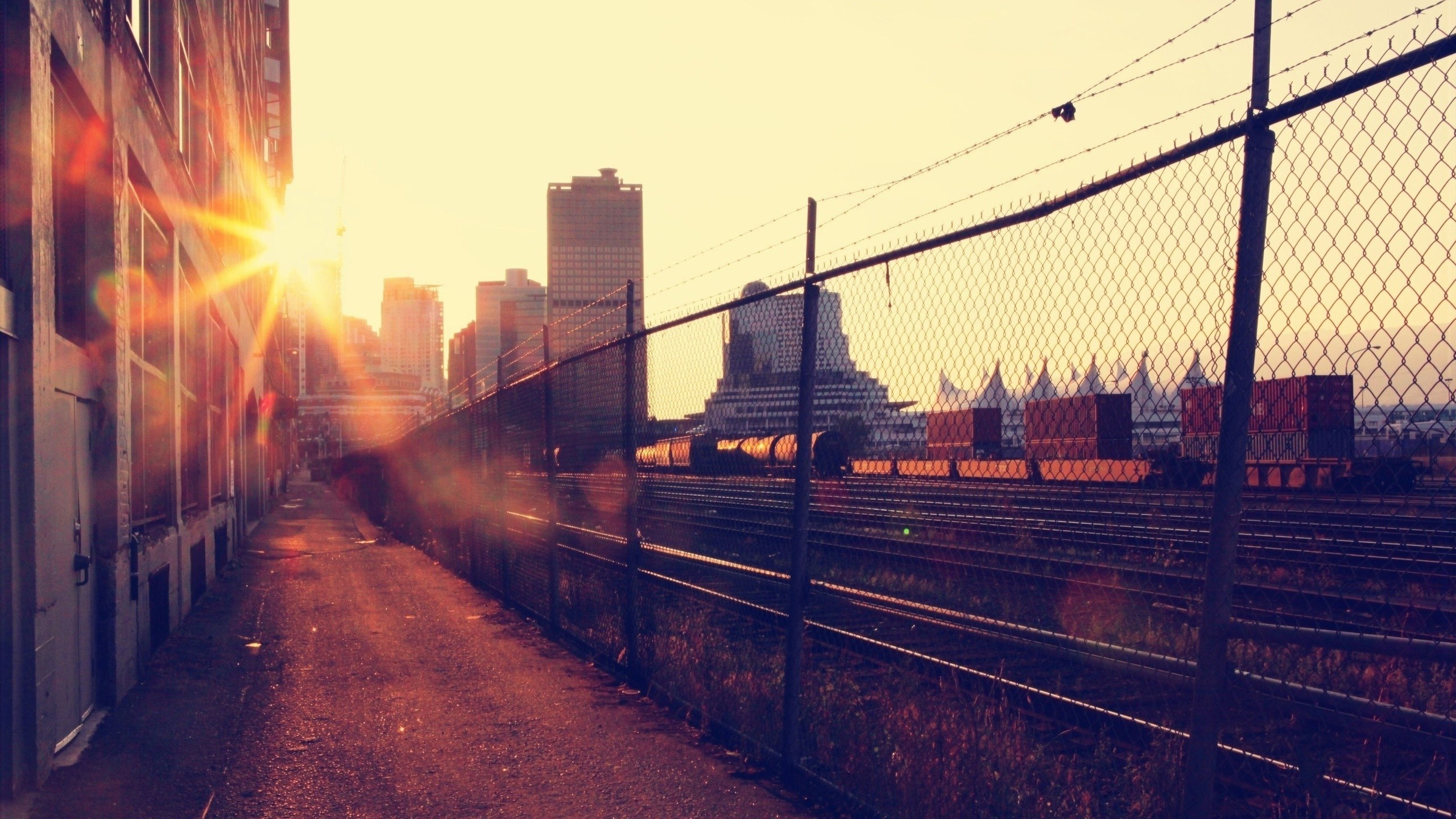 Sunset over a rail yard with cityscape and train cars HD Wallpaper