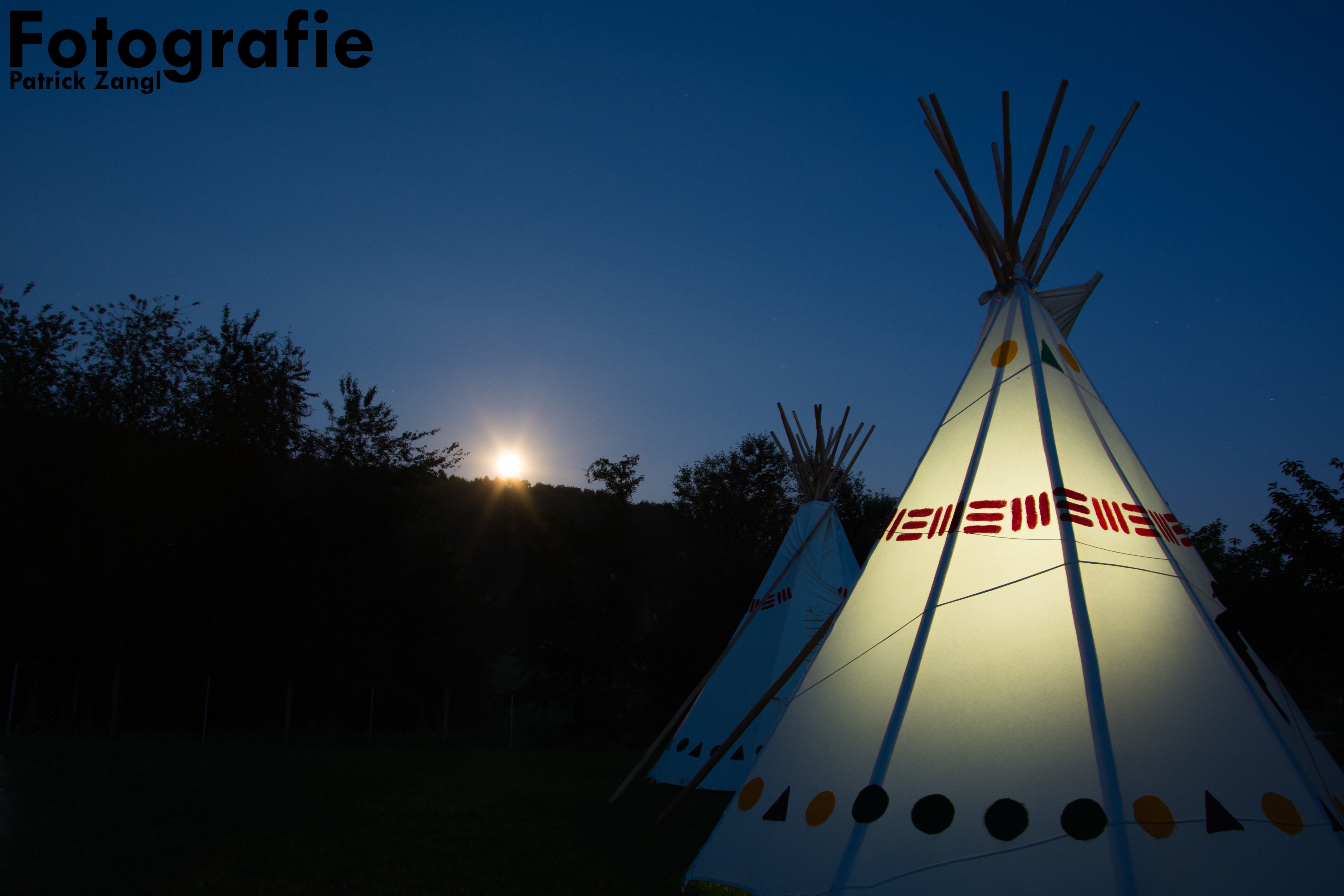 Two illuminated teepees at night with a moonlit sky HD Wallpaper
