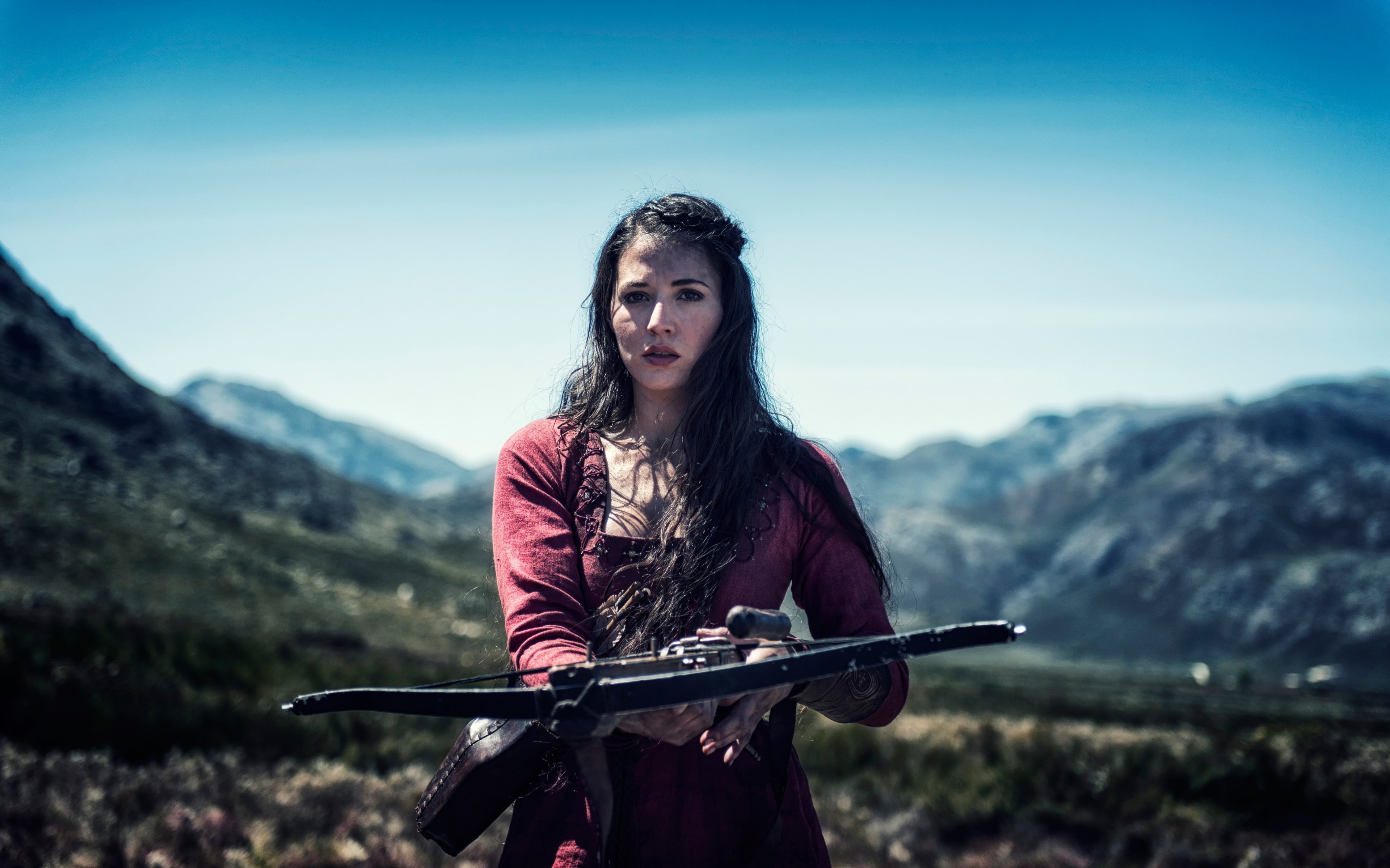 Woman holding a crossbow in a mountainous landscape HD Wallpaper