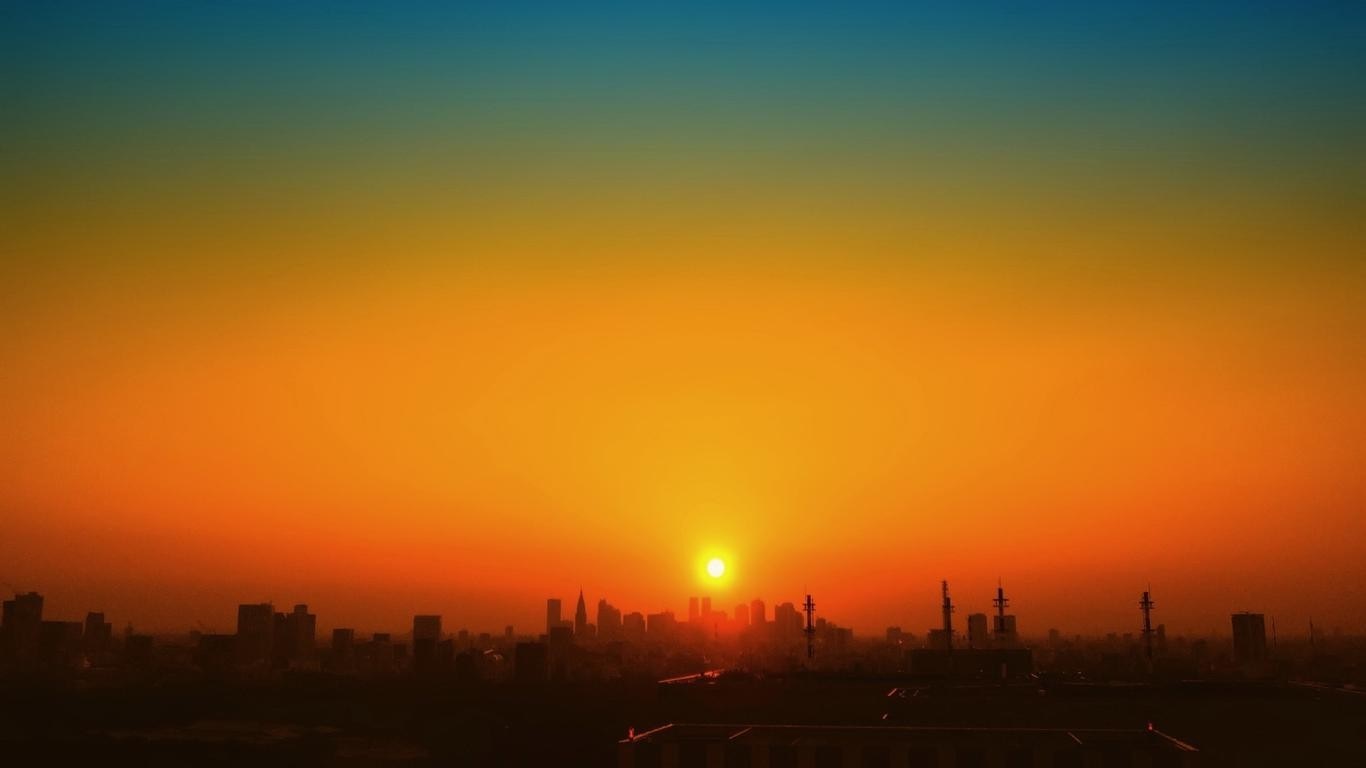 Sunset over a city skyline with orange and blue sky HD Wallpaper