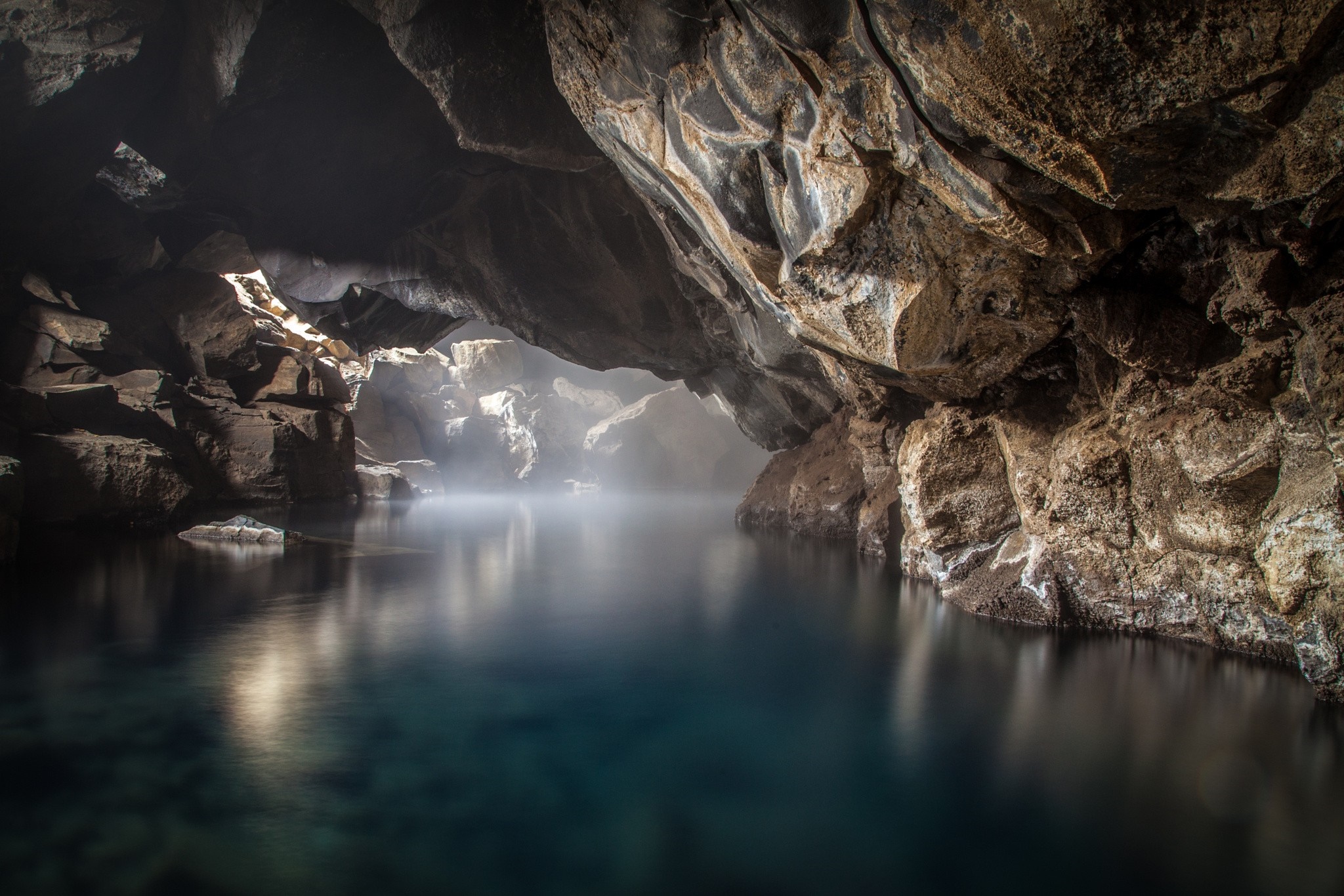 Sunlight filtering into a cave with a body of water HD Wallpaper