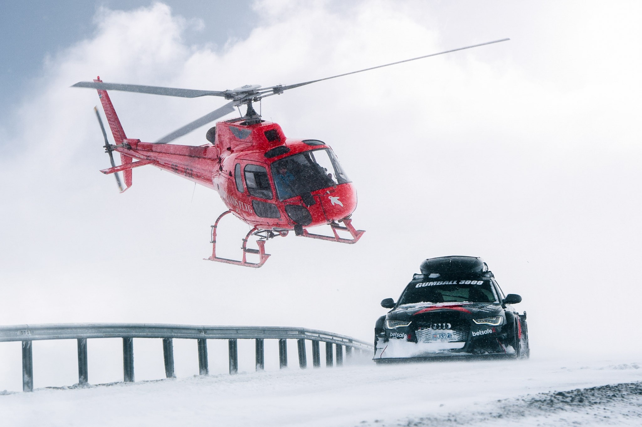 Red helicopter flying over Audi RS6 Avant in snow HD Wallpaper