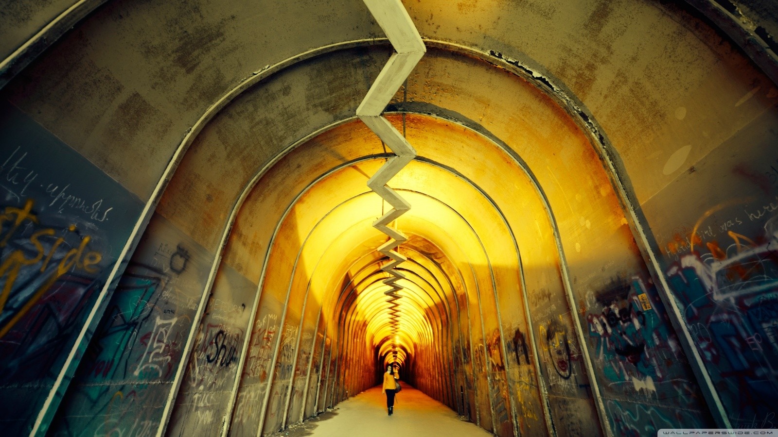 Person walking through a graffiti-covered tunnel with a zigzag ceiling HD Wallpaper