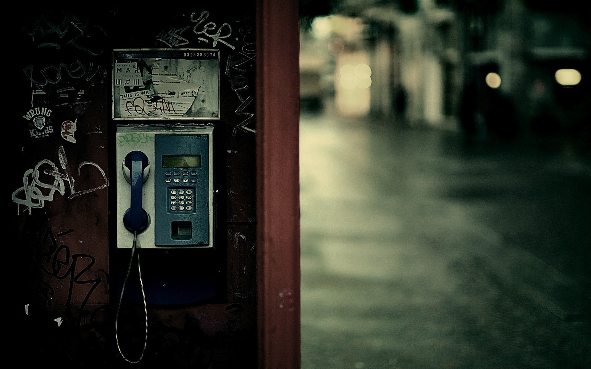 Graffiti-covered payphone on a dark city street at night HD Wallpaper