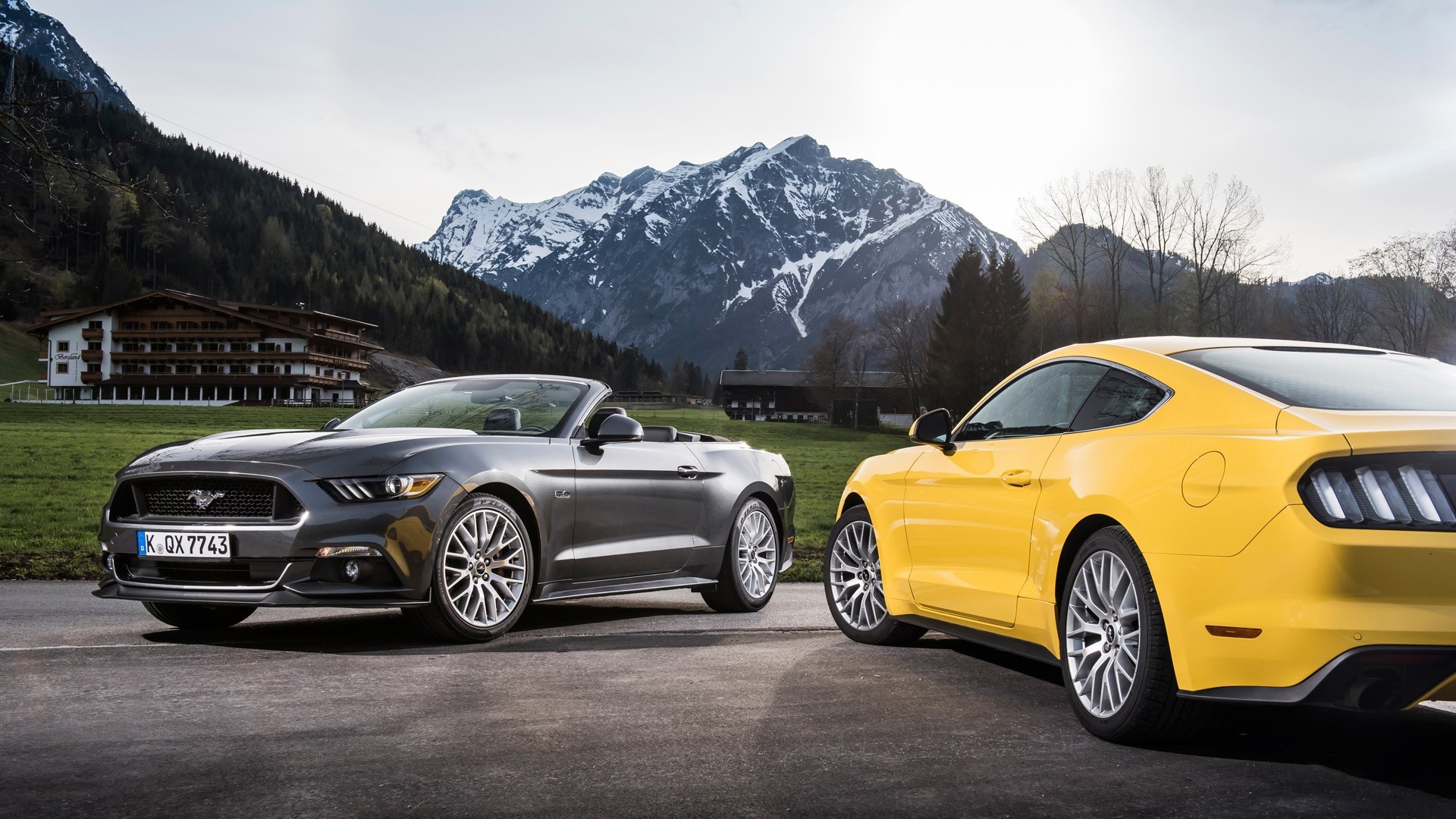 Two Ford Mustangs parked in front of a mountain hotel HD Wallpaper