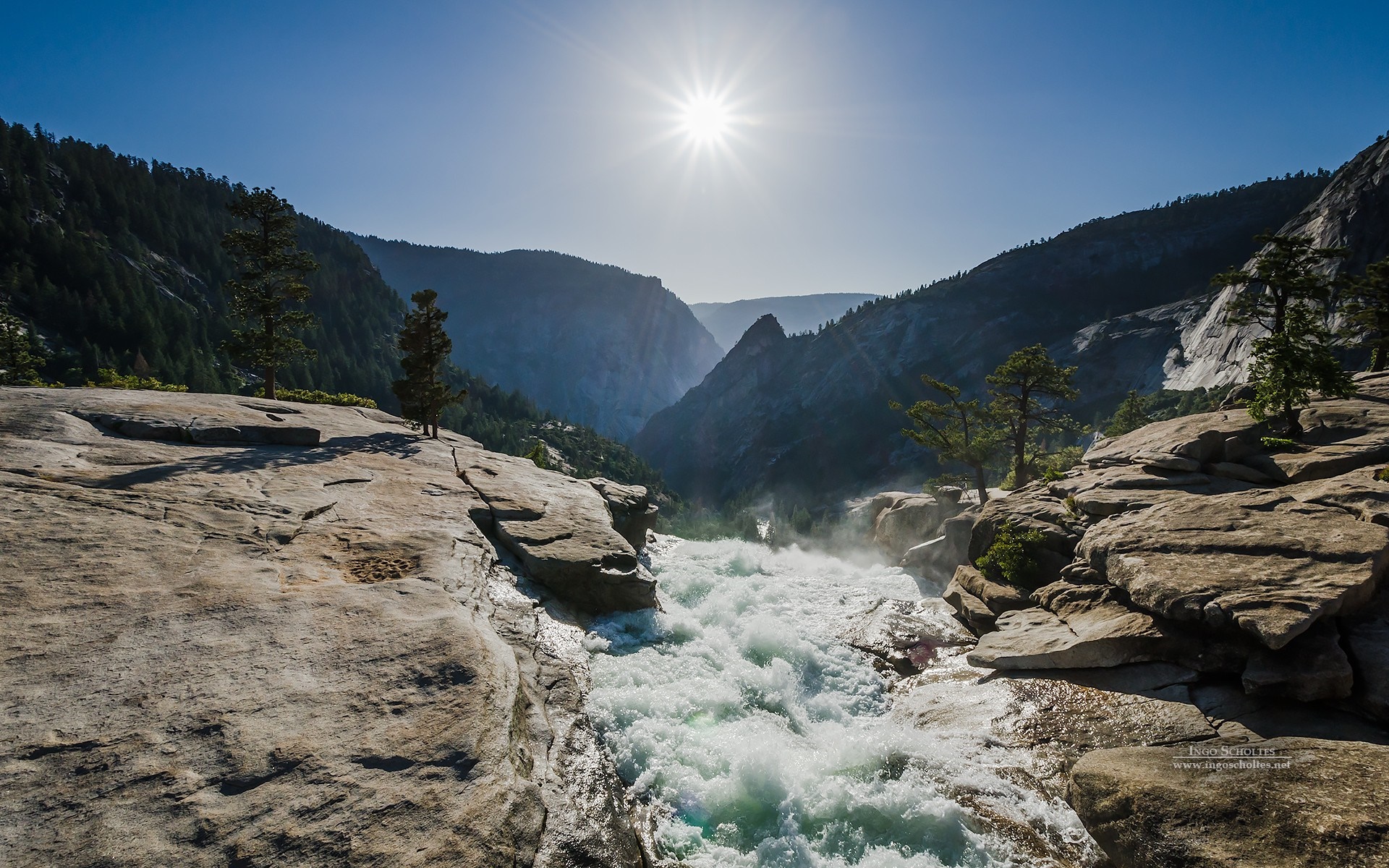 Waterfall flowing through a rocky valley under a bright sun HD Wallpaper