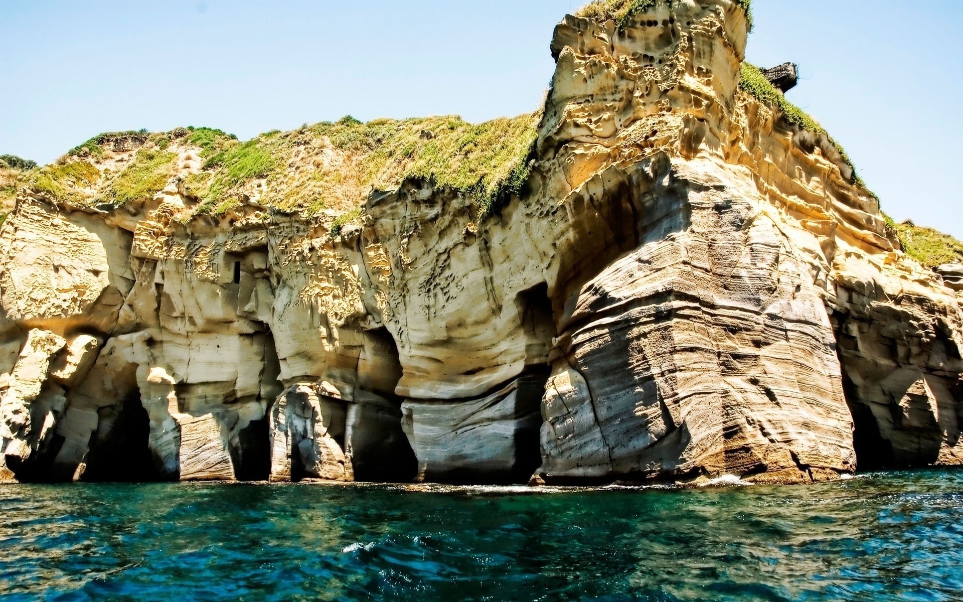 Coastal cliffs with sea caves and green vegetation HD Wallpaper