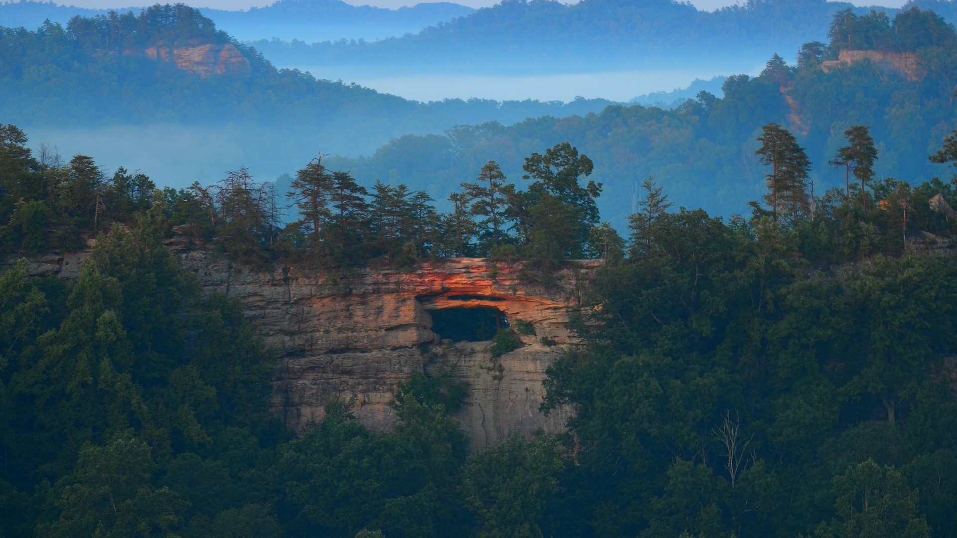 Misty valley with a natural rock arch and forest HD Wallpaper