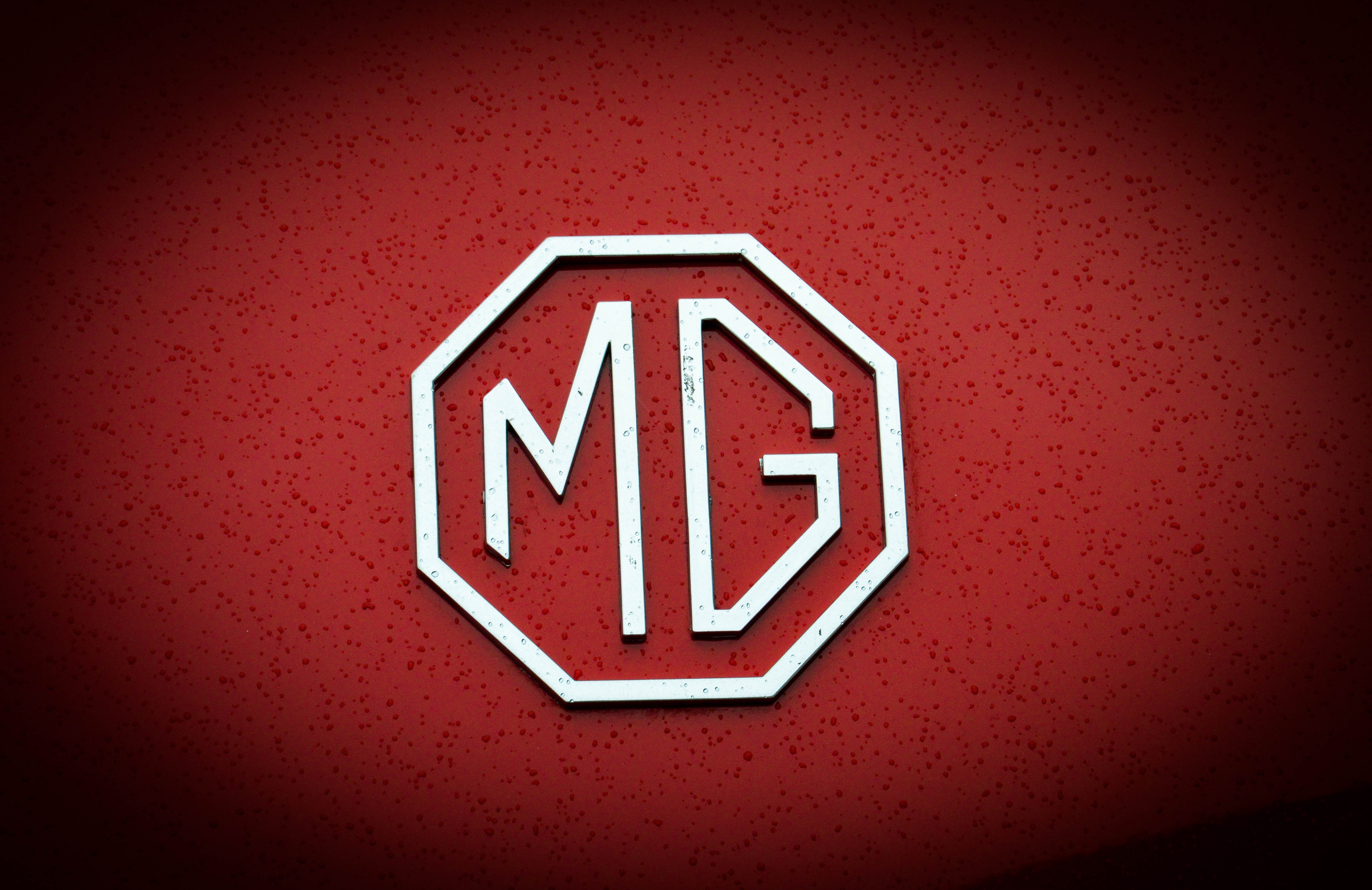 MG logo on a red car with water droplets HD Wallpaper