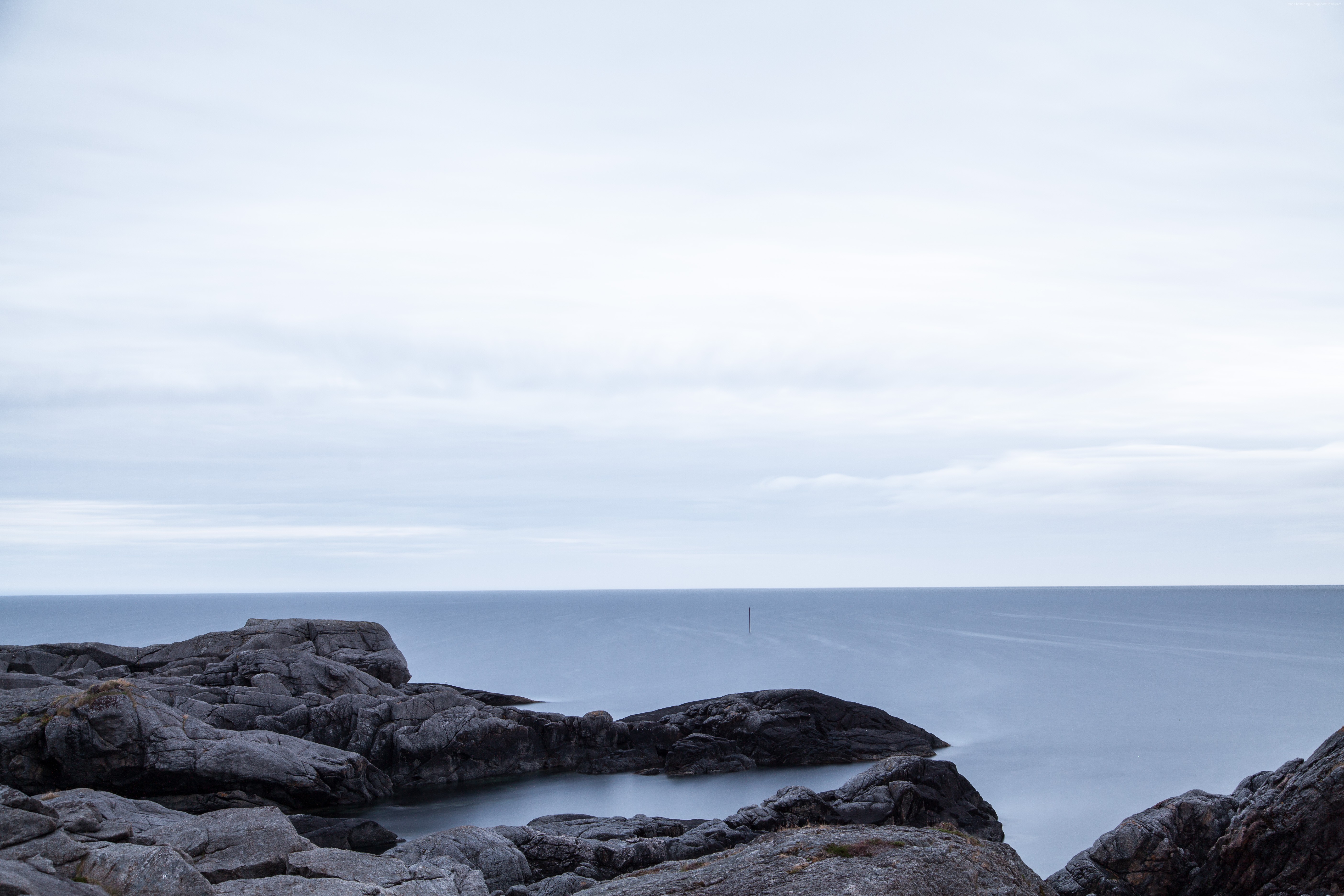 Rocky coastline overlooking a calm sea under a cloudy sky HD Wallpaper