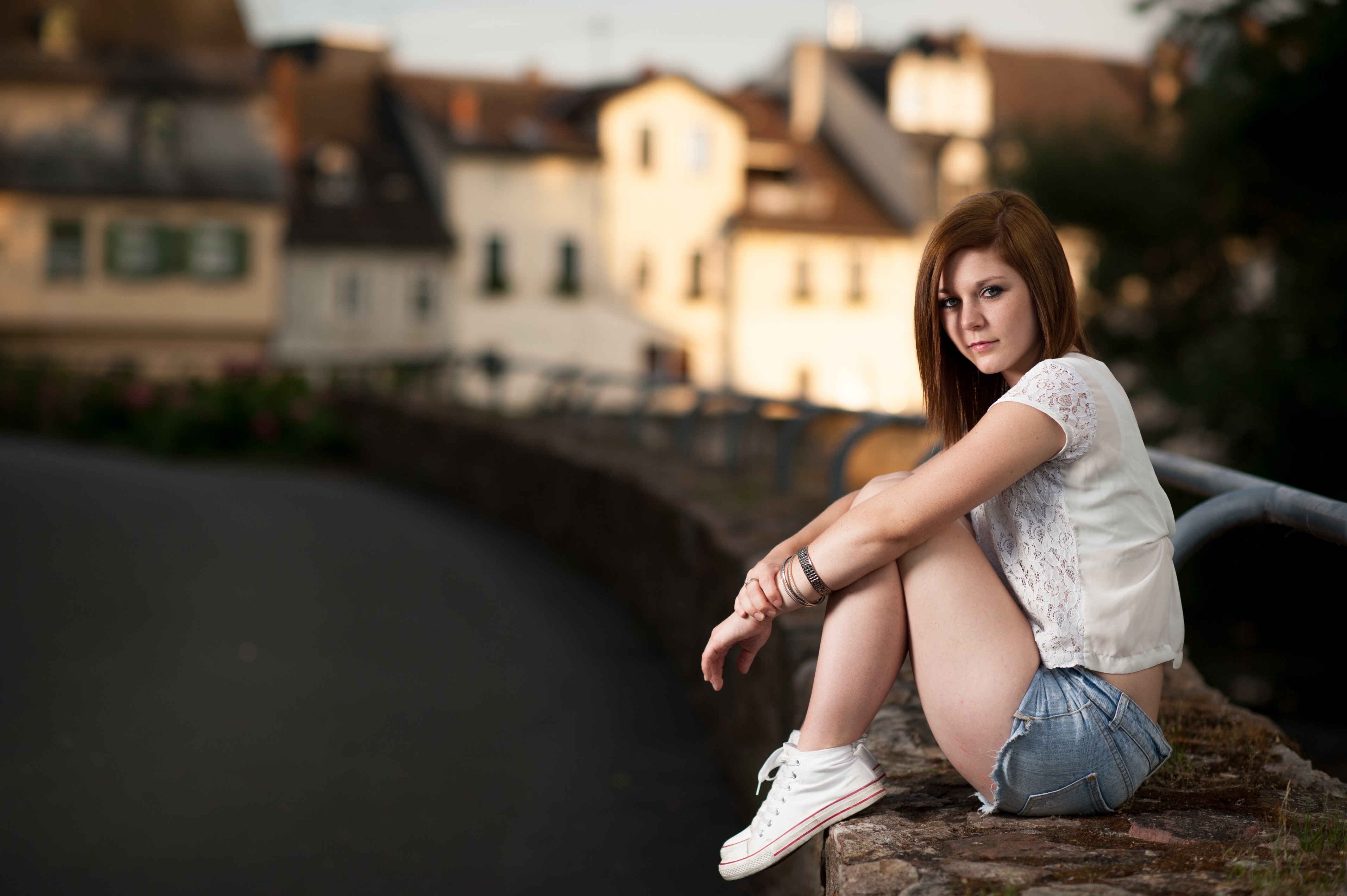 Woman sitting on a stone wall in front of buildings HD Wallpaper