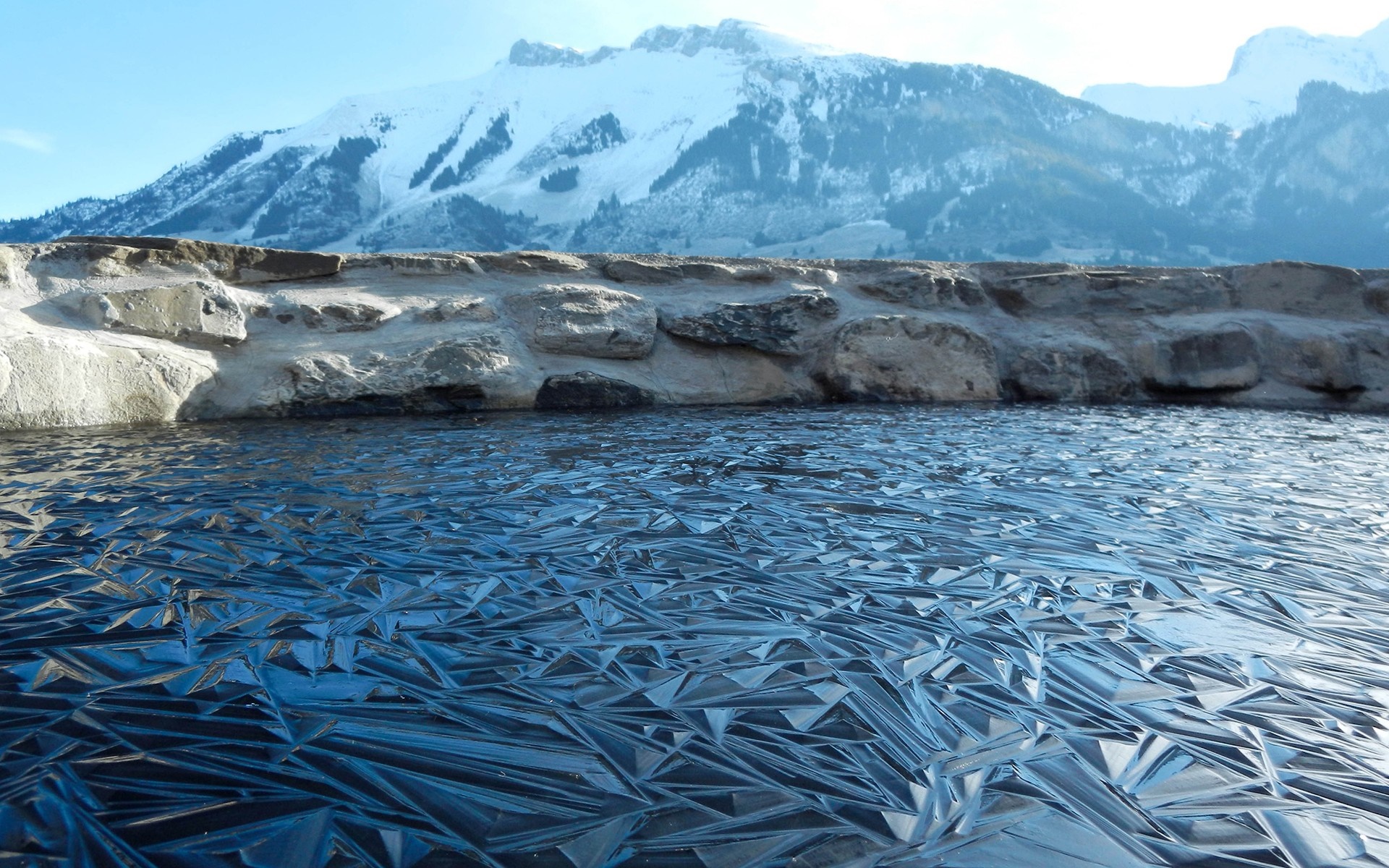 Frozen lake with ice patterns and snow-capped mountains HD Wallpaper
