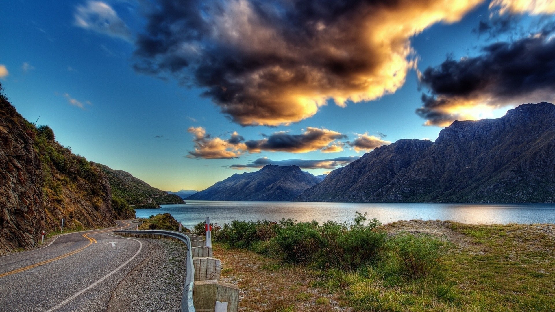 Winding road along a lake with mountains at sunset HD Wallpaper