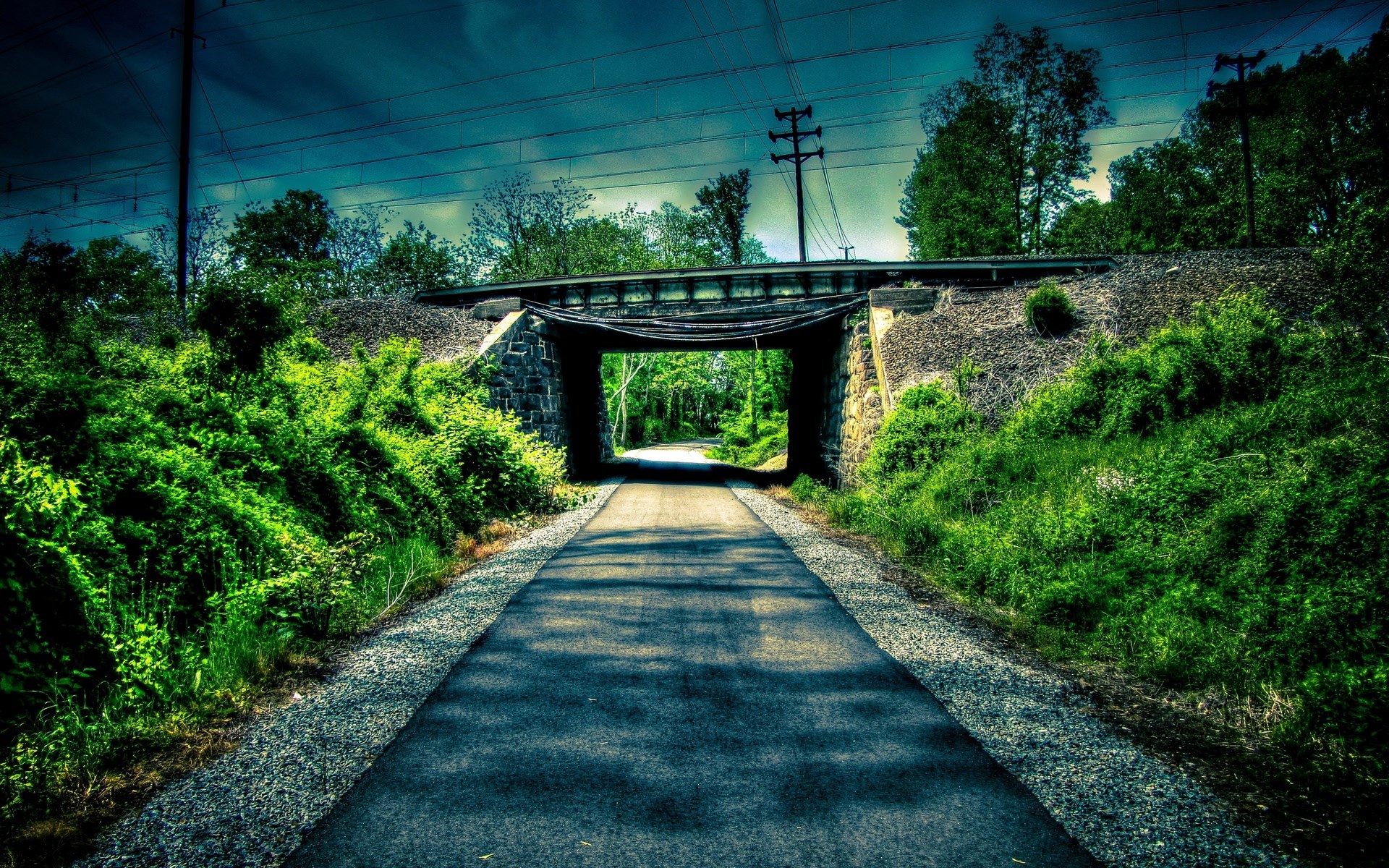 A paved path goes under a stone bridge with trees HD Wallpaper
