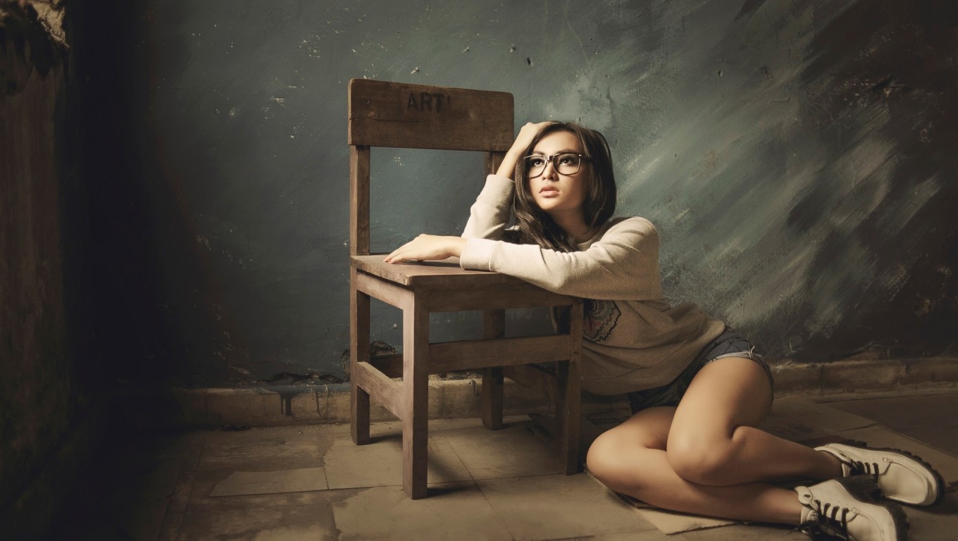Woman with glasses sitting by a chair HD Wallpaper