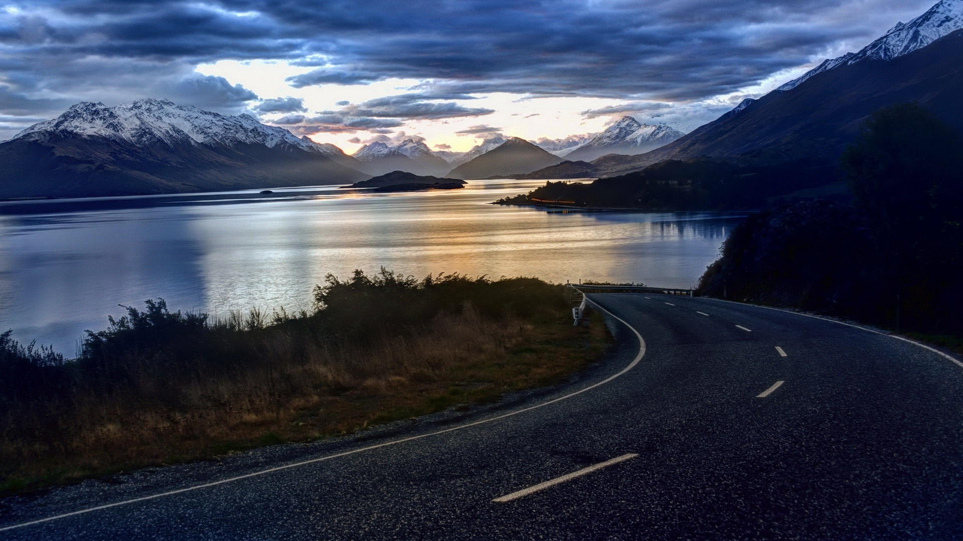 Winding road by a lake with snow-capped mountains at dawn HD Wallpaper
