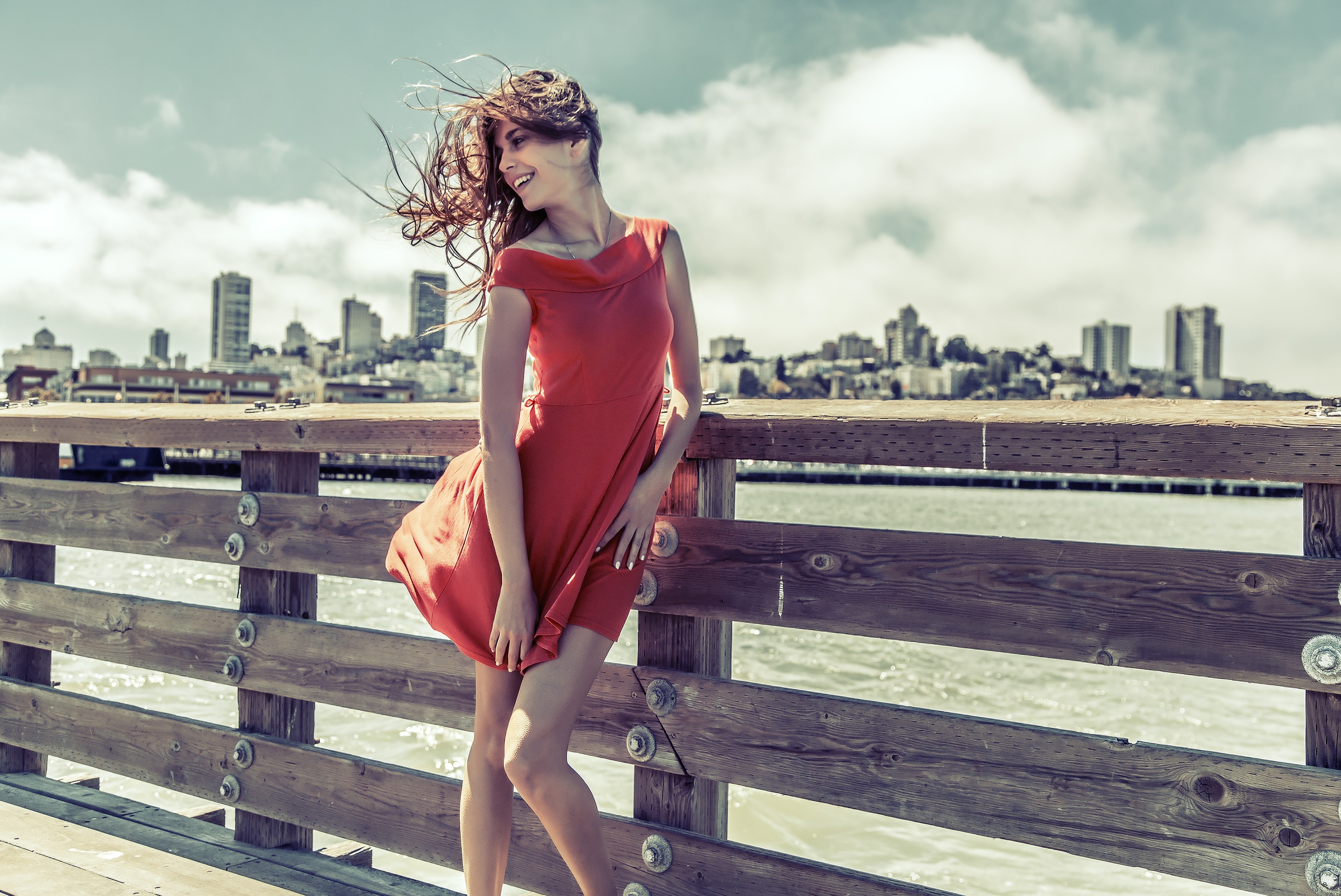 Woman in red dress on pier with city skyline HD Wallpaper