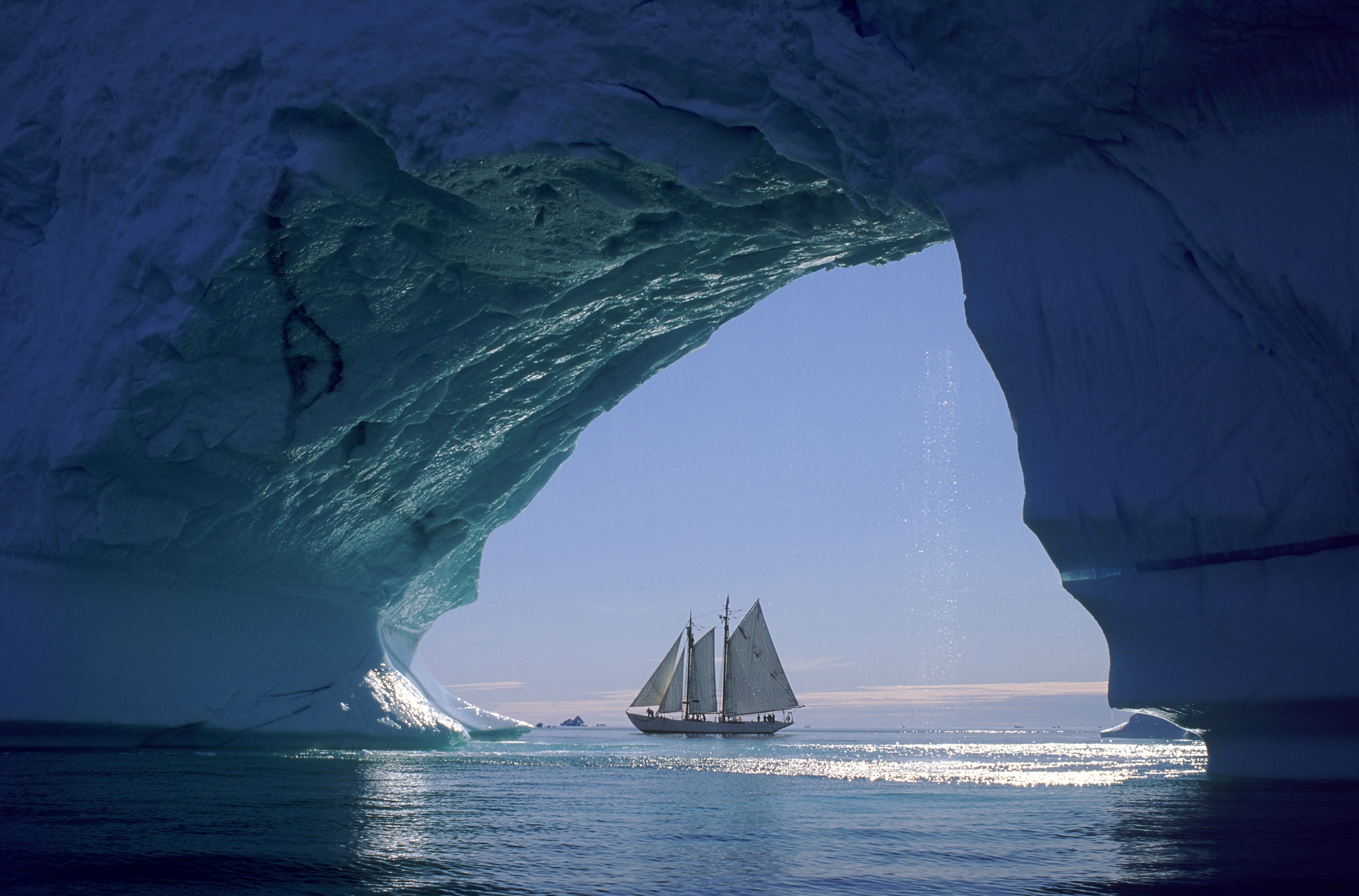 Sailboat passes through an iceberg cave in the Arctic Ocean HD Wallpaper