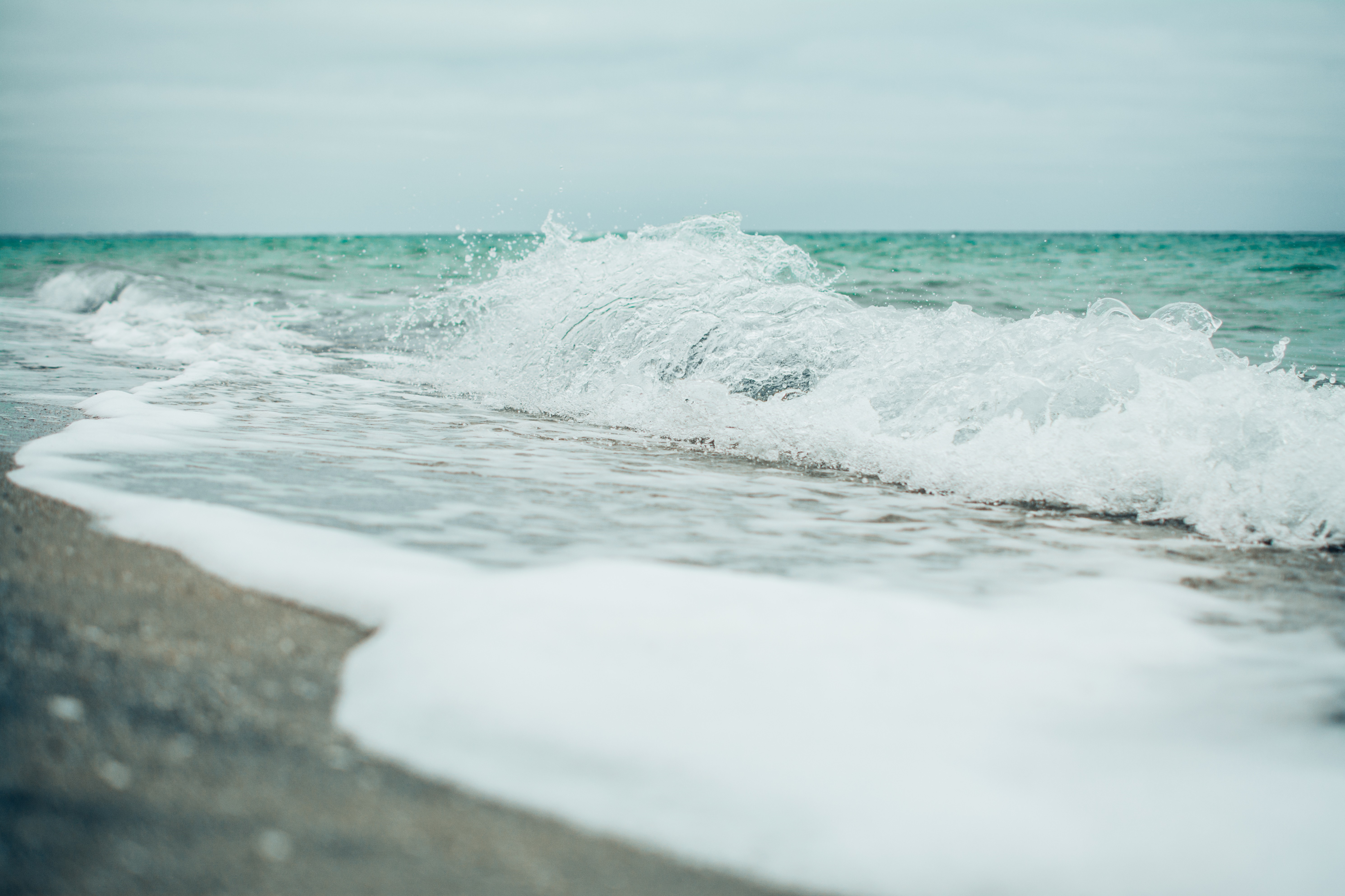 Ocean wave crashing on a sandy beach HD Wallpaper