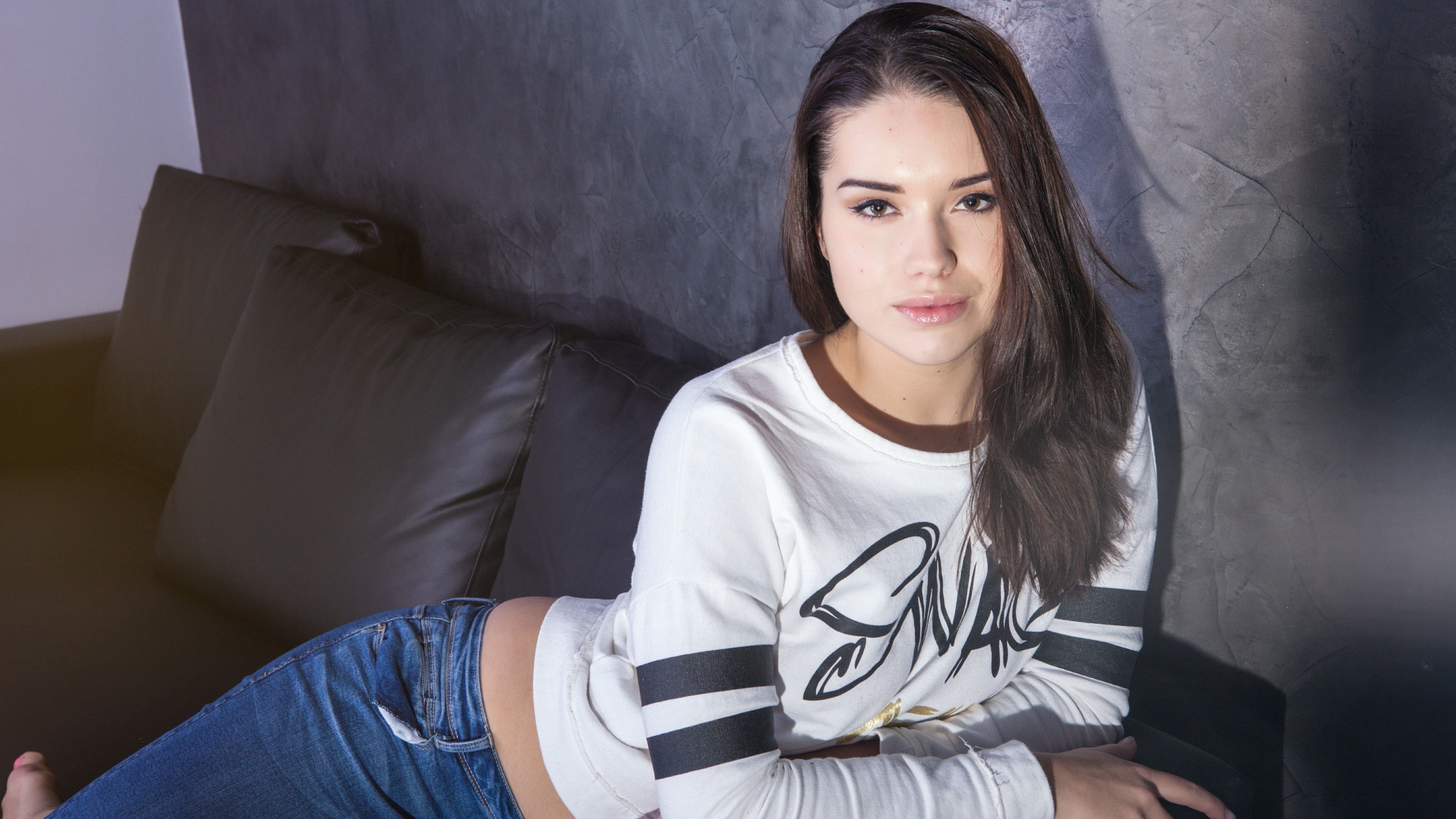 Woman in white shirt and jeans sitting on a couch HD Wallpaper