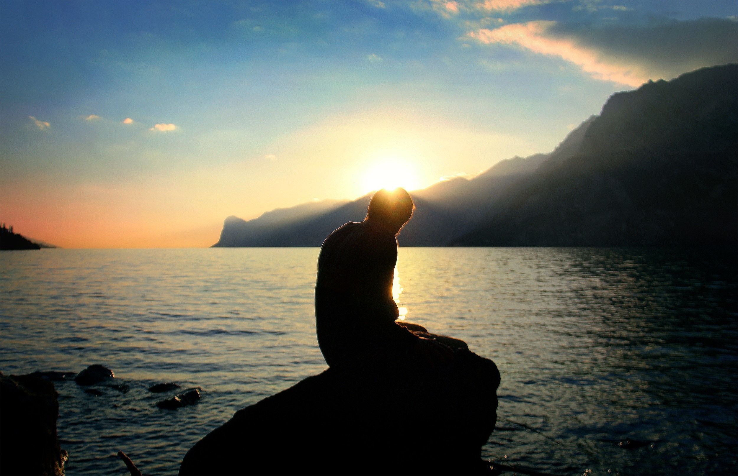 Silhouette of a person sitting on a rock at sunset by the sea HD Wallpaper