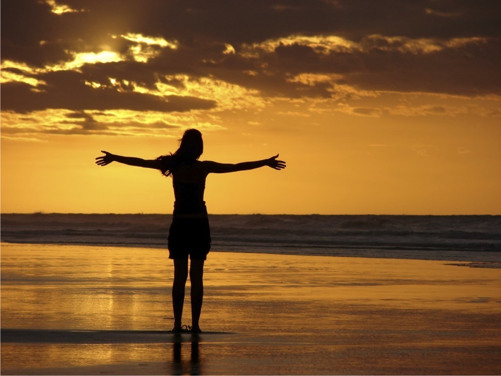 Silhouette of a woman with arms outstretched on a beach at sunset HD Wallpaper