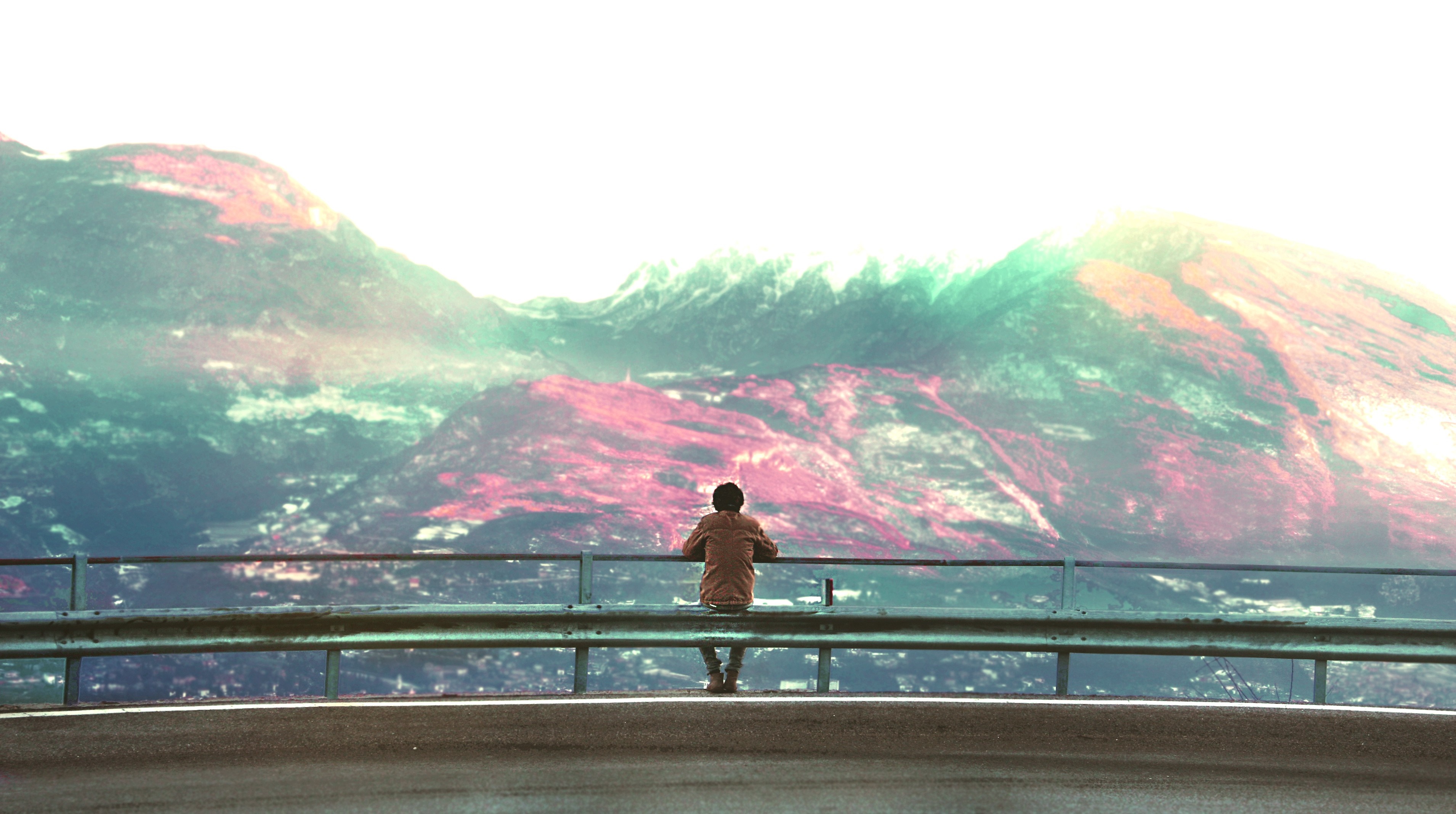 Person sitting on a guardrail overlooking mountains HD Wallpaper