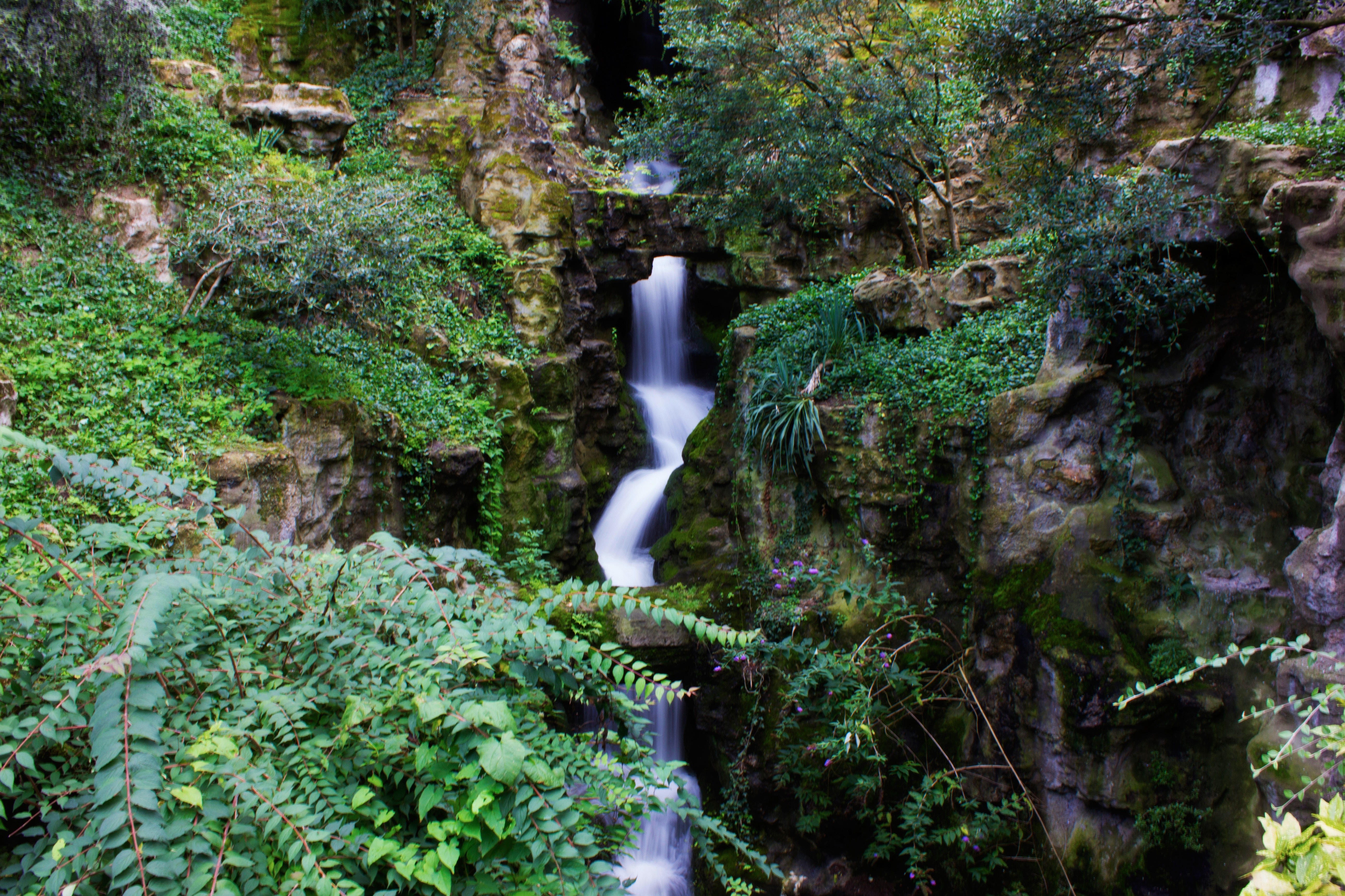 Waterfall cascading through a rocky, overgrown garden HD Wallpaper