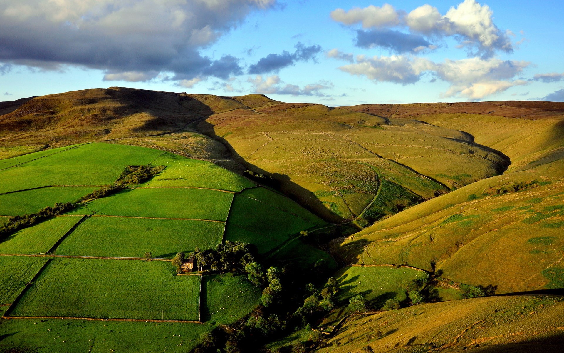 Rolling hills with green fields and a valley HD Wallpaper