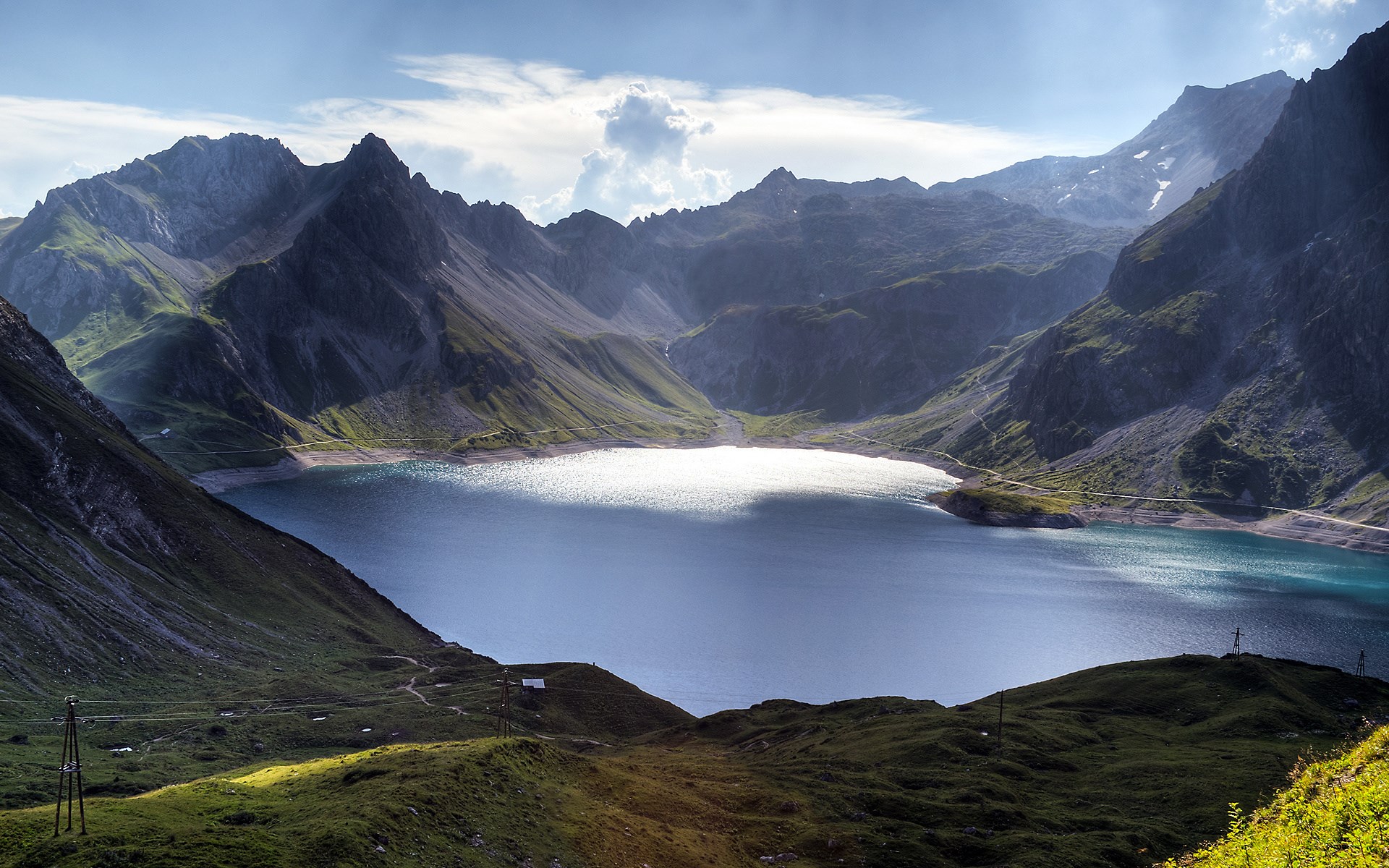 Mountain lake with sunlit water and rocky peaks HD Wallpaper