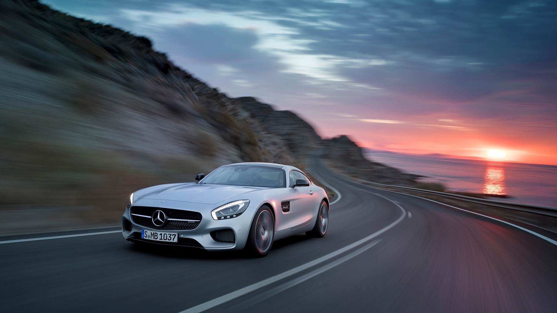 Silver Mercedes-Benz AMG GT driving on coastal road at sunset HD Wallpaper