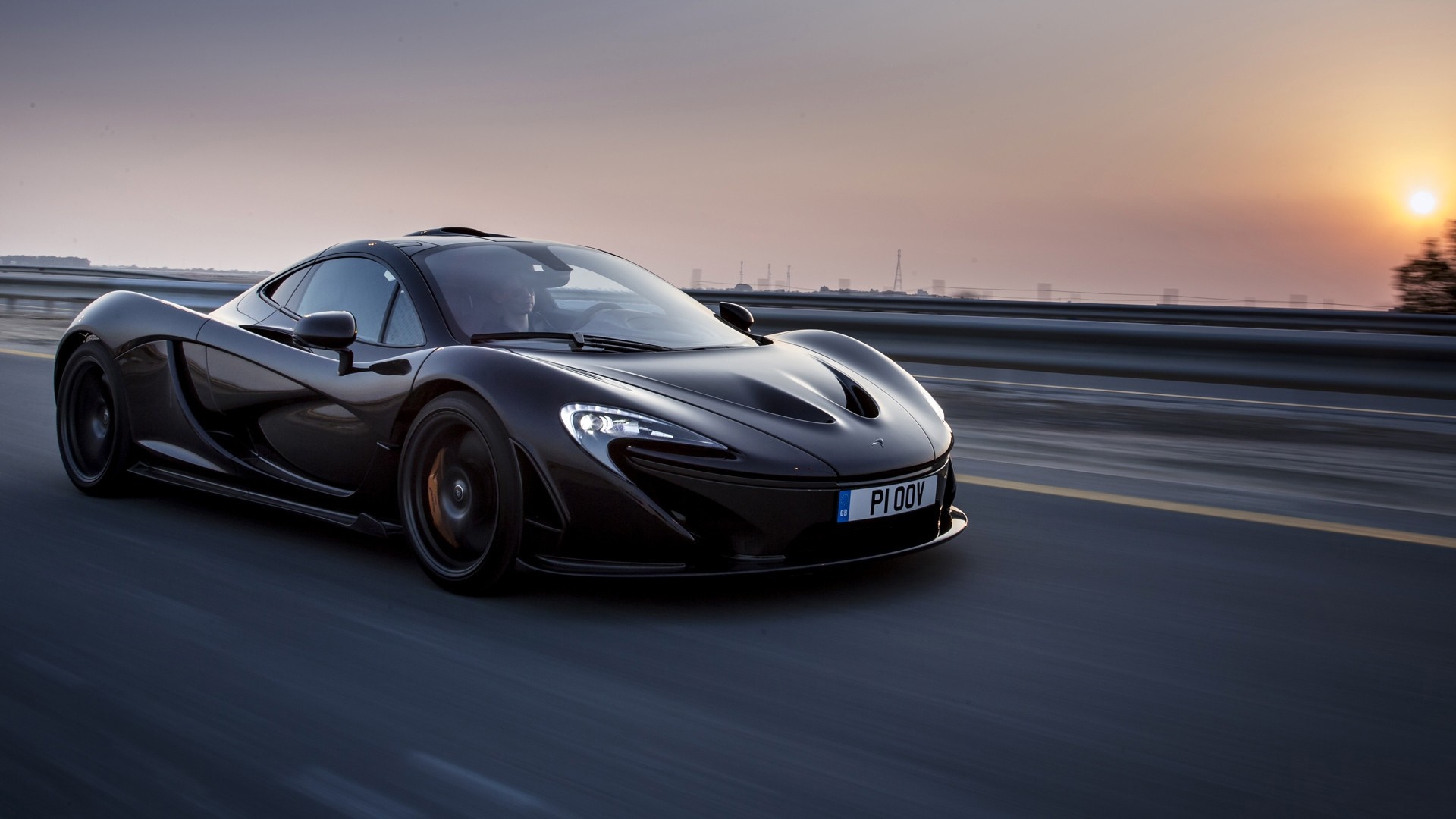 Black McLaren P1 sports car driving on a road at sunset HD Wallpaper