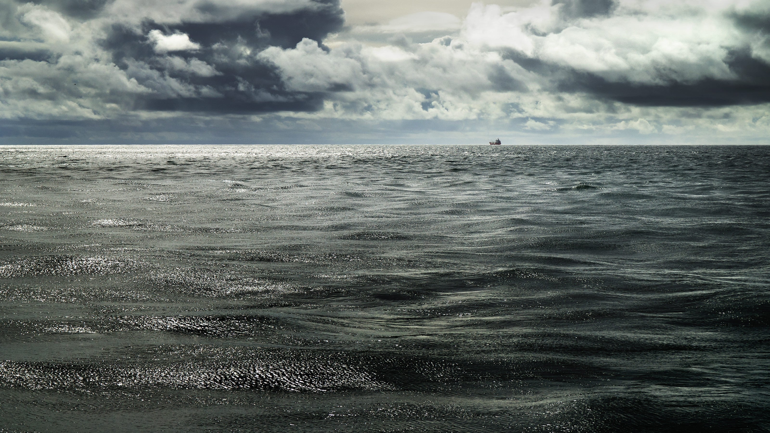 A lone ship on the horizon under stormy clouds HD Wallpaper