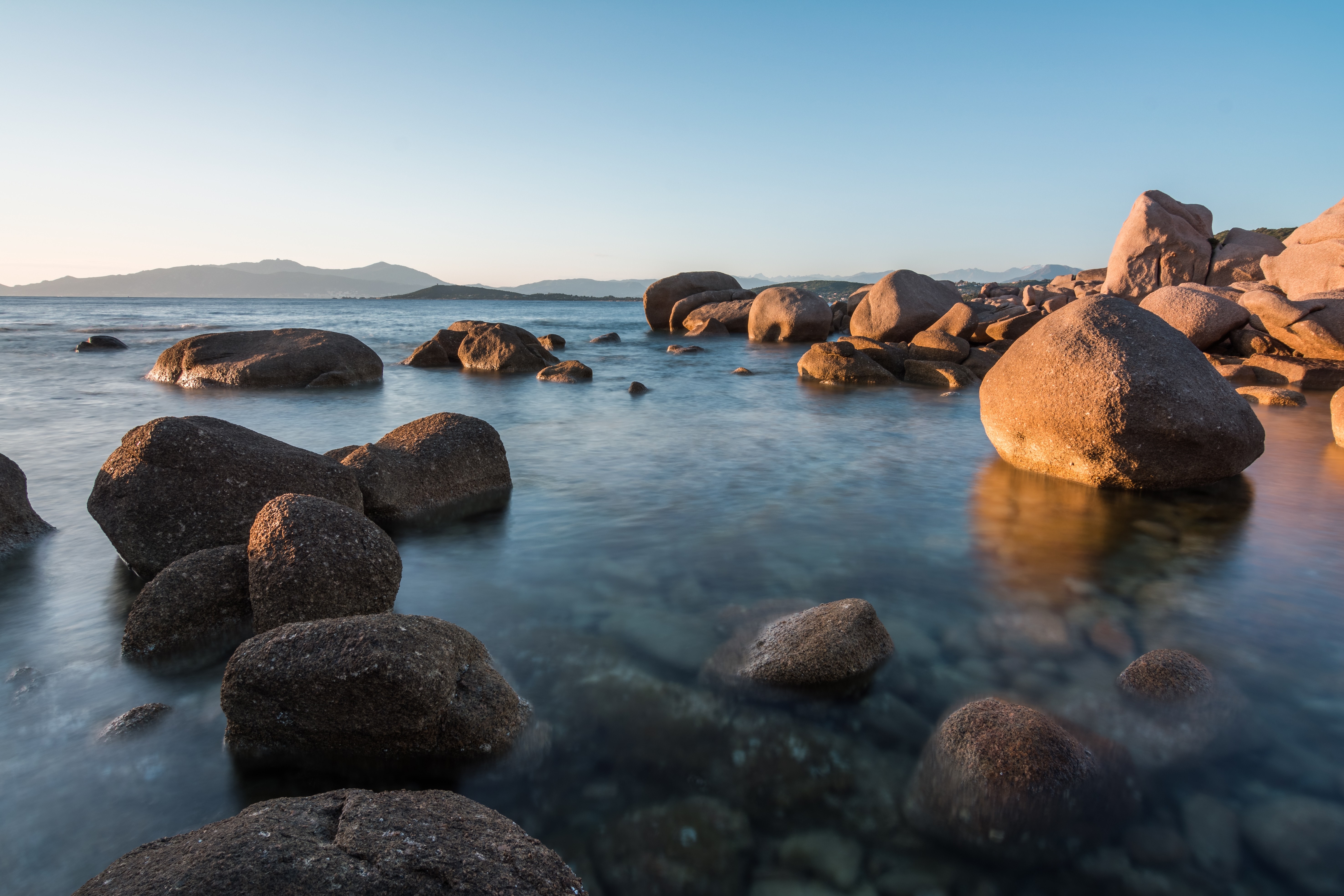 Rocky coastline at sunset with calm sea HD Wallpaper