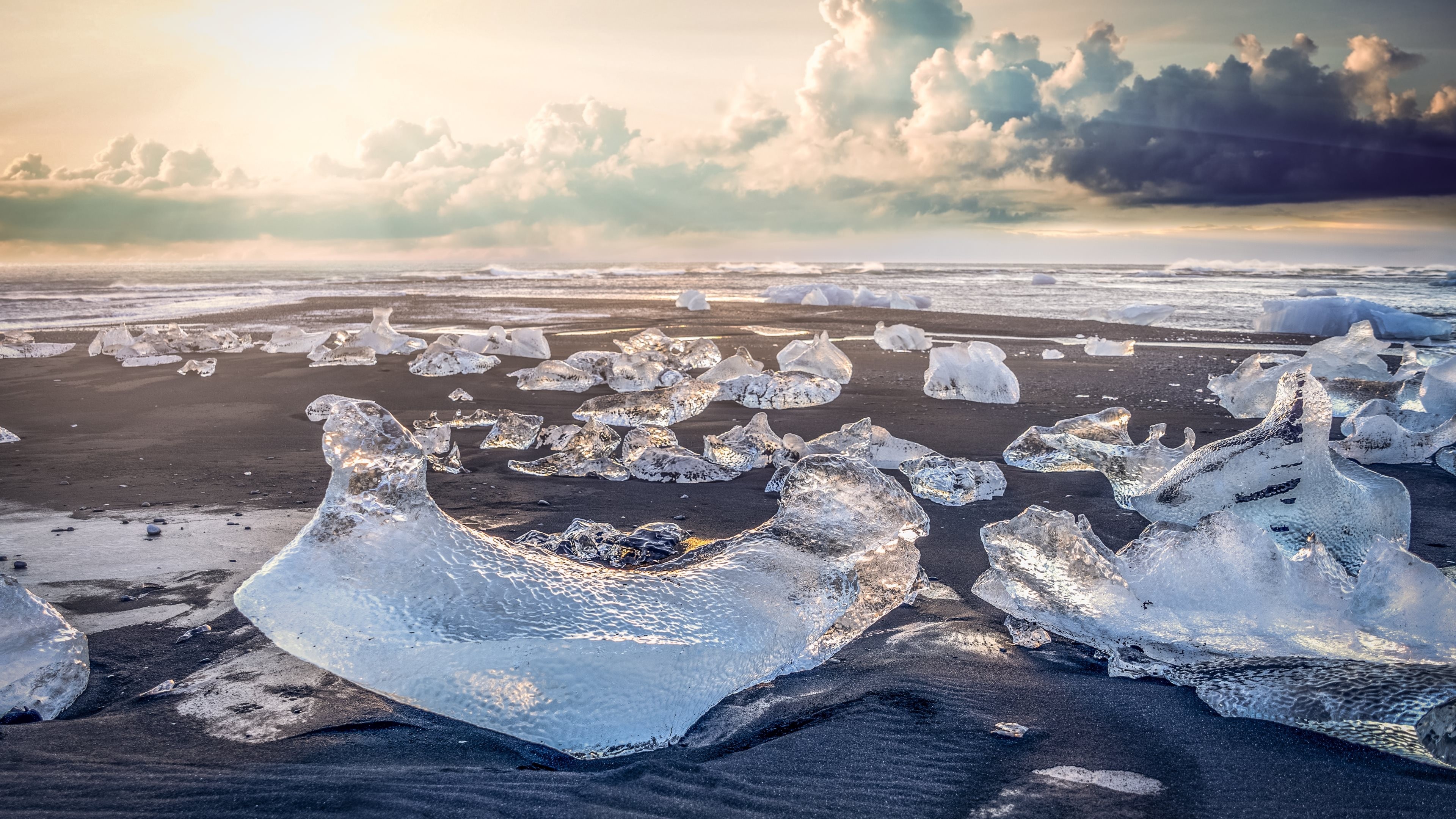 Ice chunks on a black sand beach with ocean waves and clouds HD Wallpaper