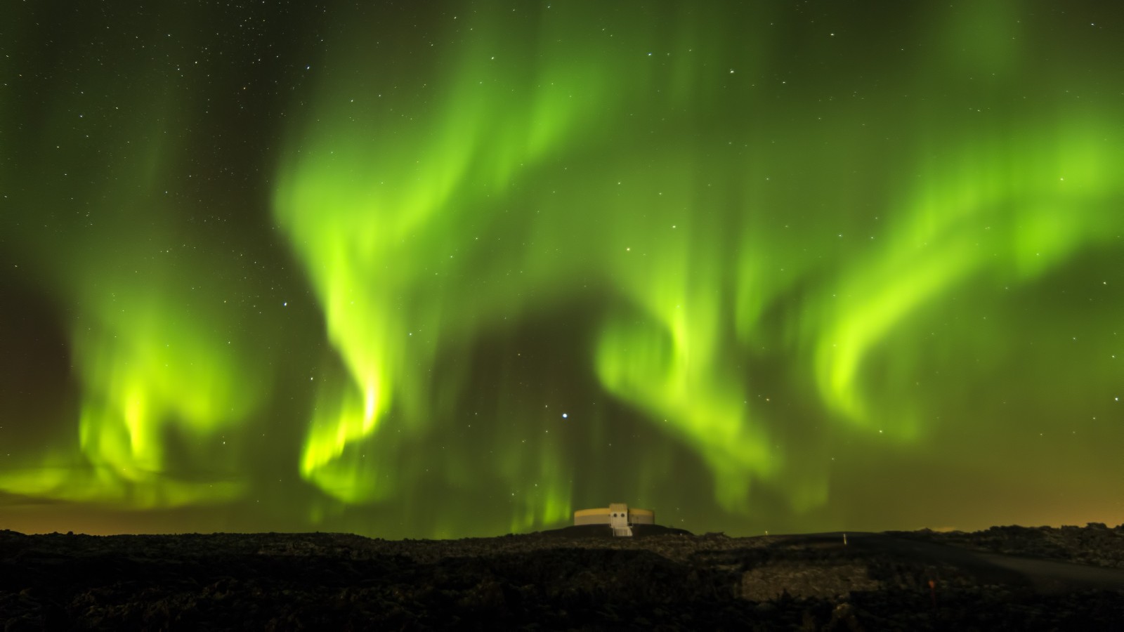 Aurora Borealis over a building in a dark landscape HD Wallpaper
