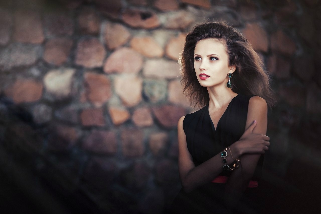 Woman with long hair and jewelry in front of stone wall HD Wallpaper