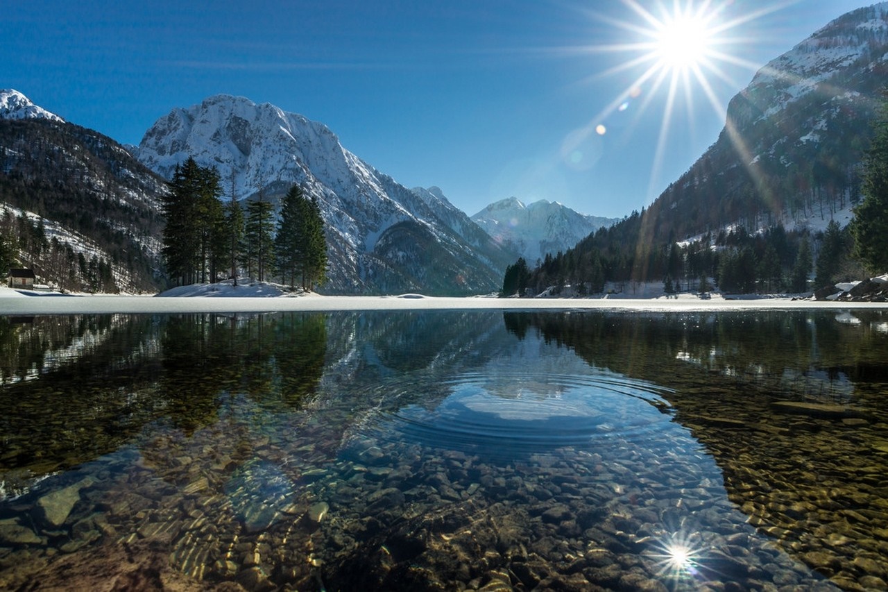 Sunlight over a snowy mountain lake with reflections HD Wallpaper