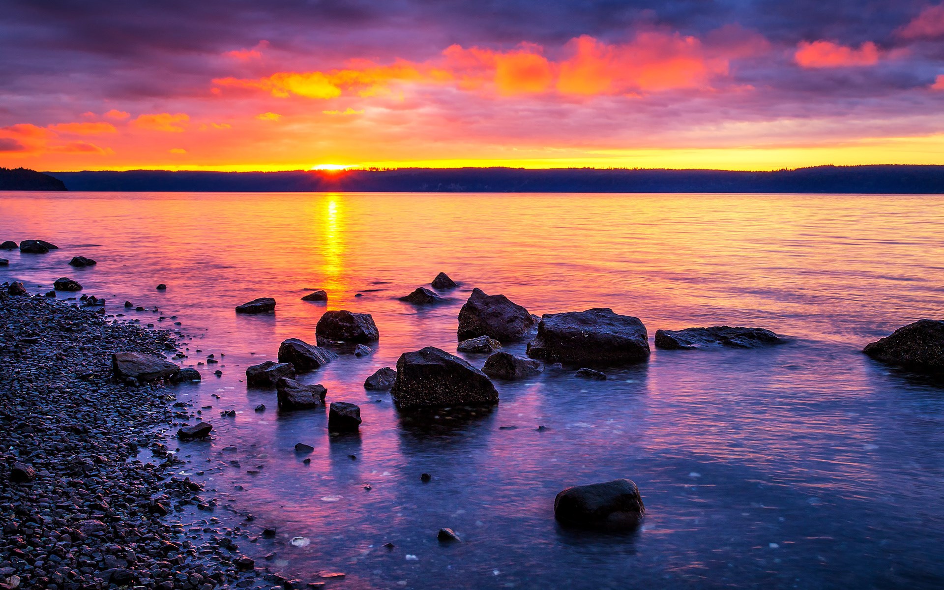 Sunset over a rocky shore with calm water HD Wallpaper