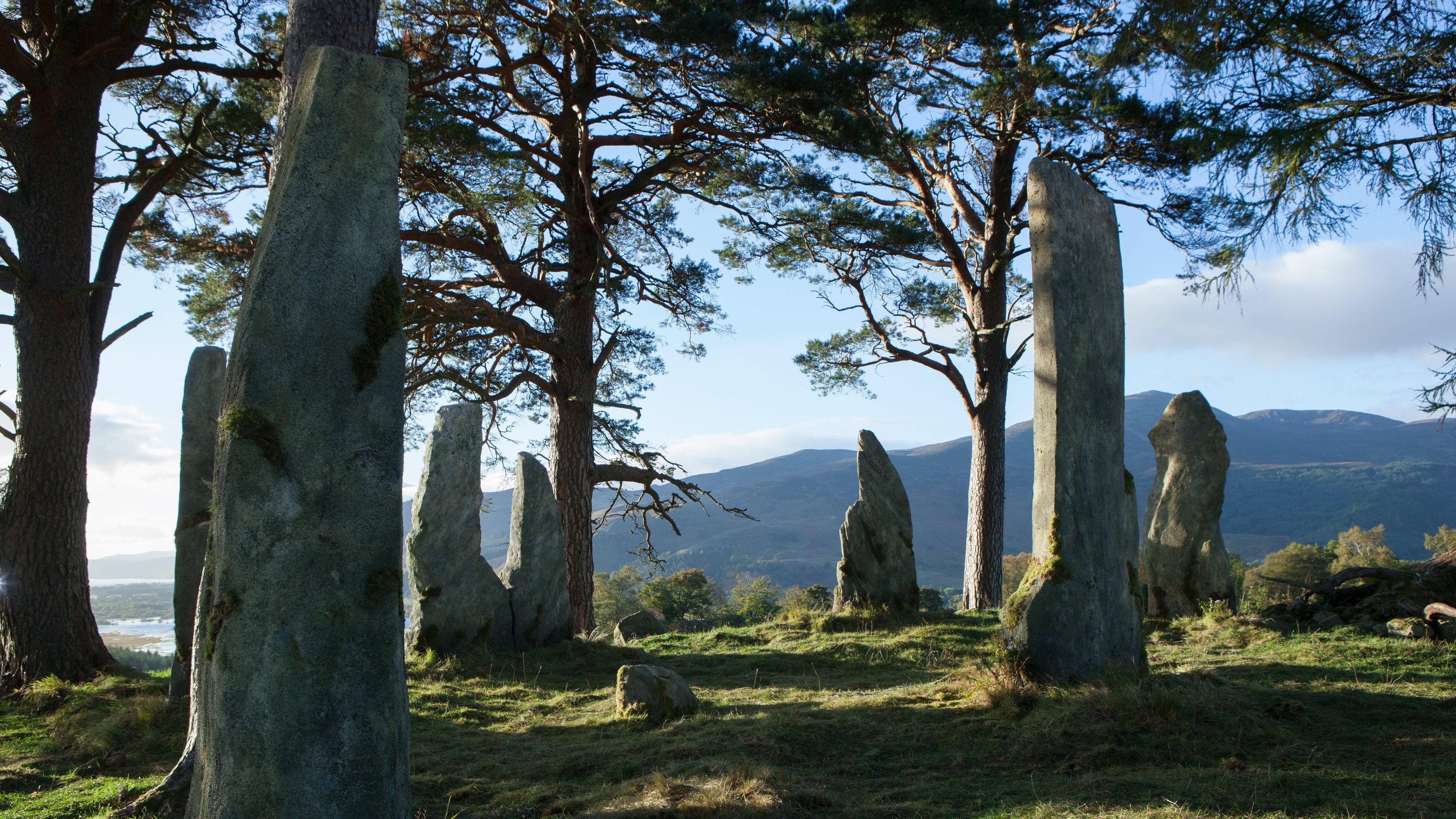 Standing stones in a wooded landscape with mountains HD Wallpaper