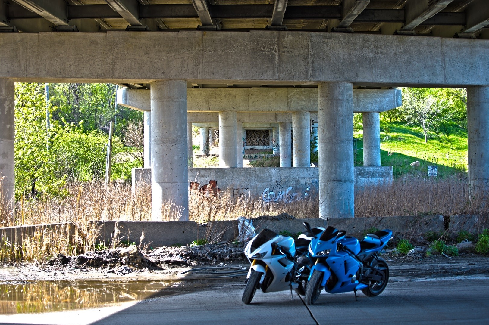 Two sport motorcycles parked under a concrete overpass HD Wallpaper
