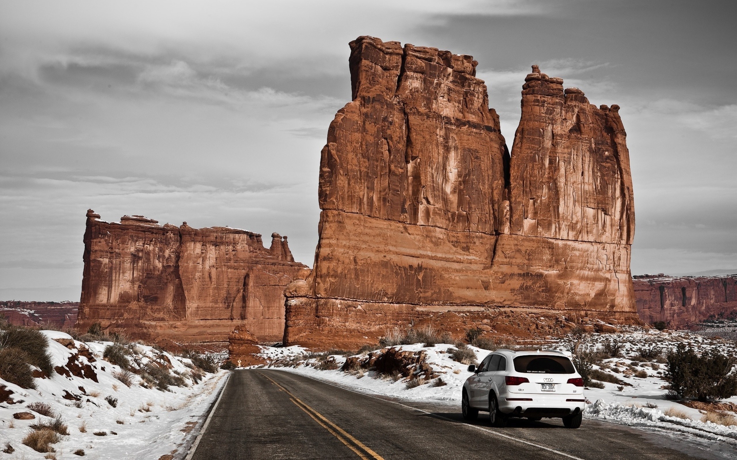White Audi driving on a snowy road past rock formations HD Wallpaper