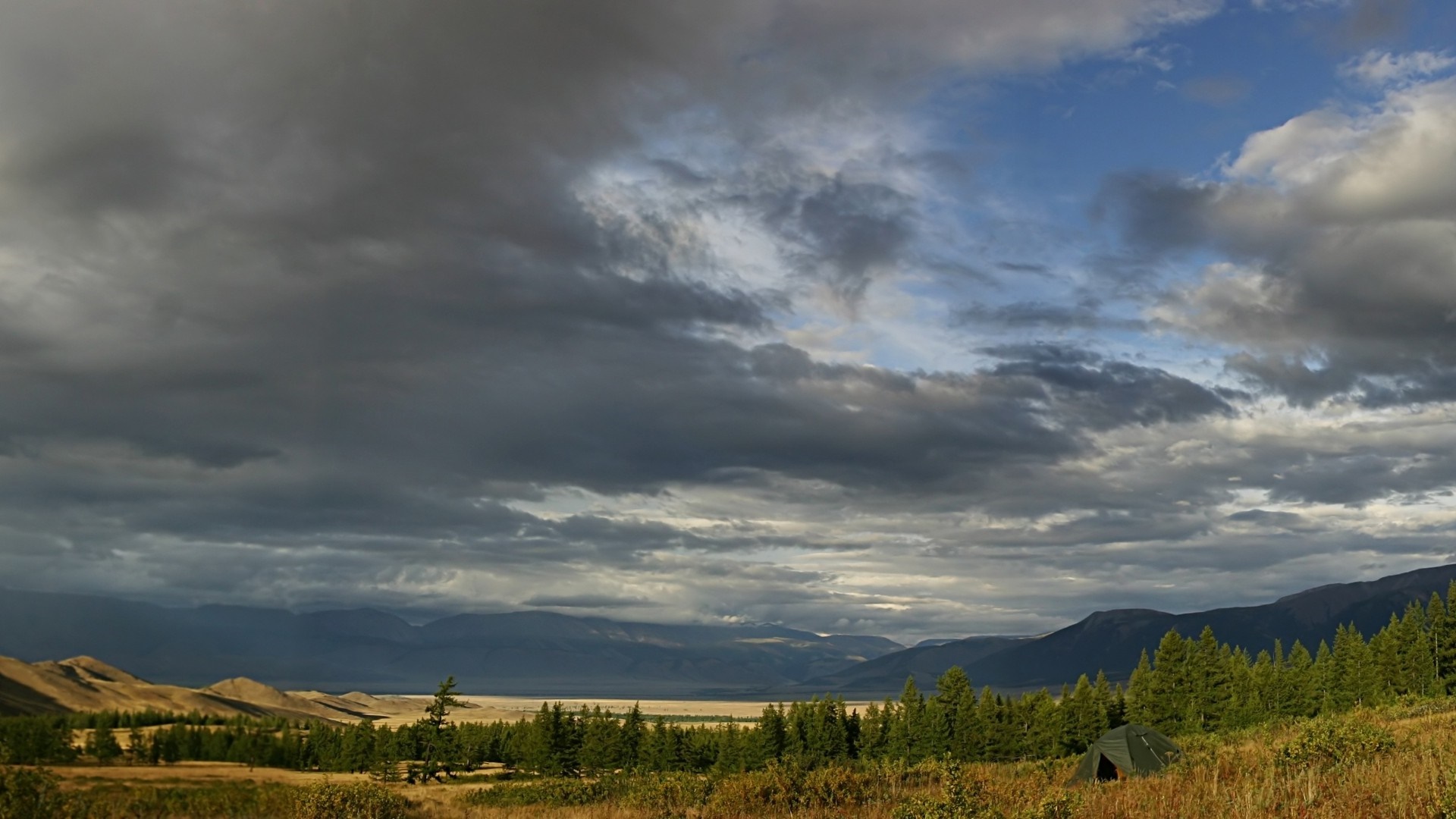 Stormy sky over a vast landscape with mountains and a tent HD Wallpaper