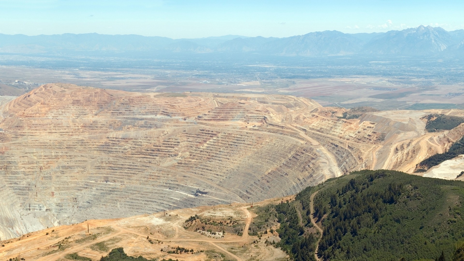 Aerial view of a massive open-pit mine with mountains in the distance HD Wallpaper