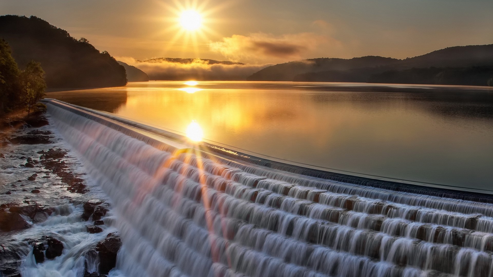 Sunrise over a dam with water cascading down HD Wallpaper
