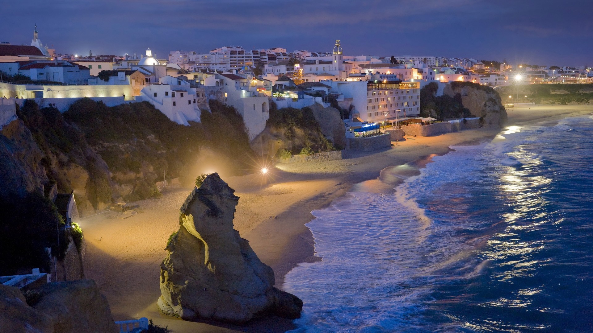 Coastal town at night with waves crashing on the beach HD Wallpaper