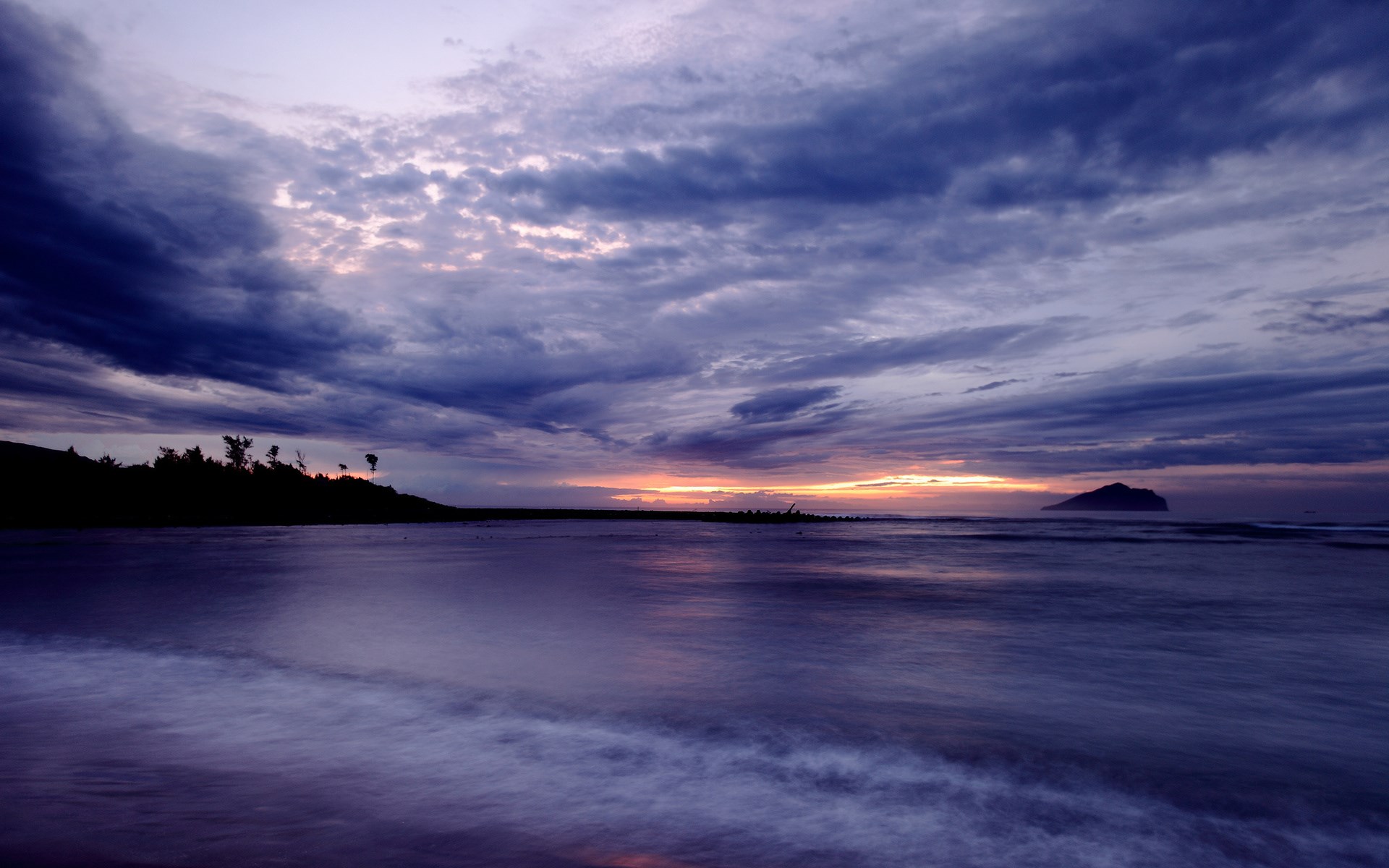 Ocean waves at sunset with dark clouds and island HD Wallpaper