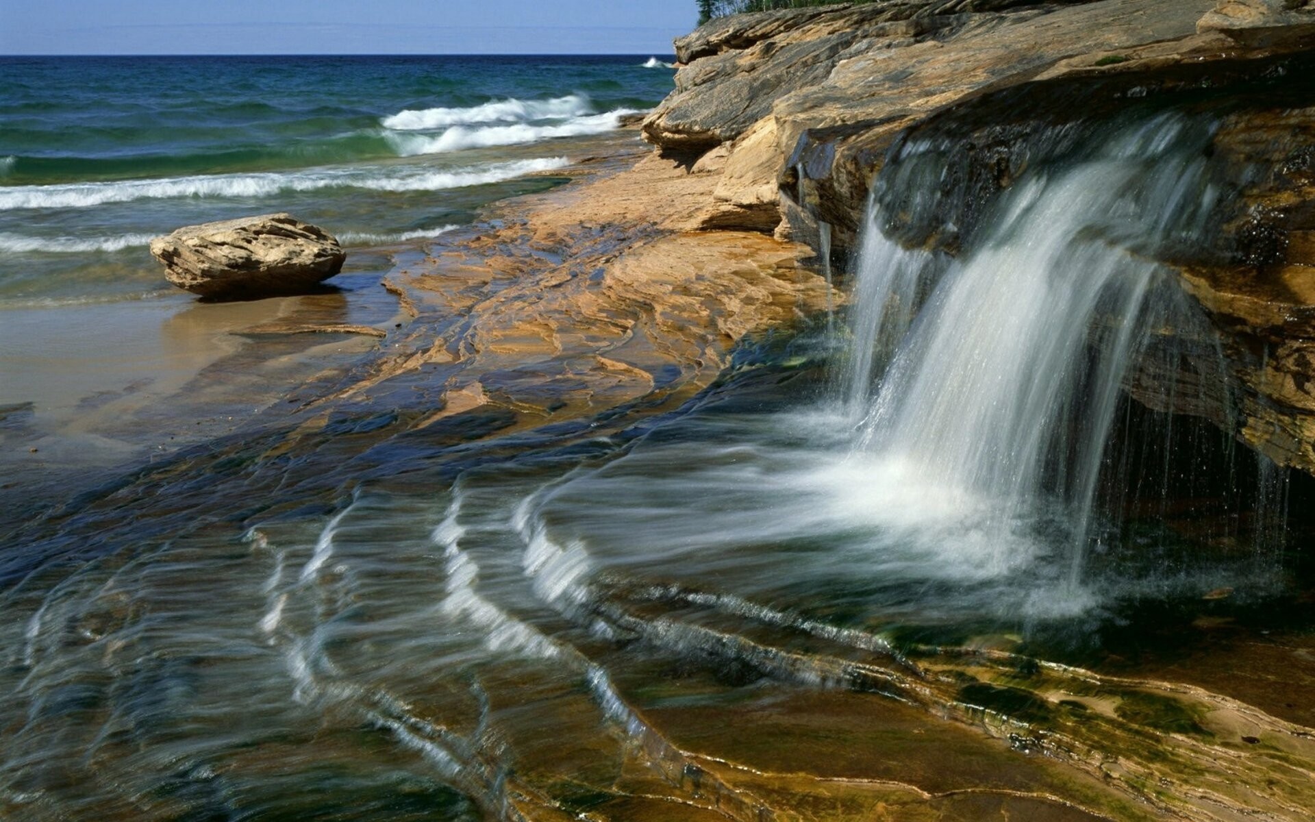 Waterfall cascading over rocks into the sea HD Wallpaper