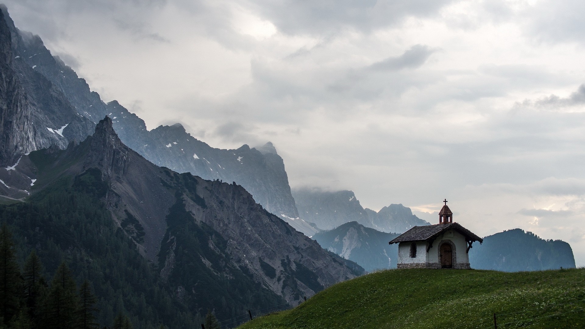 Small church on a grassy hill with mountains in the background HD Wallpaper